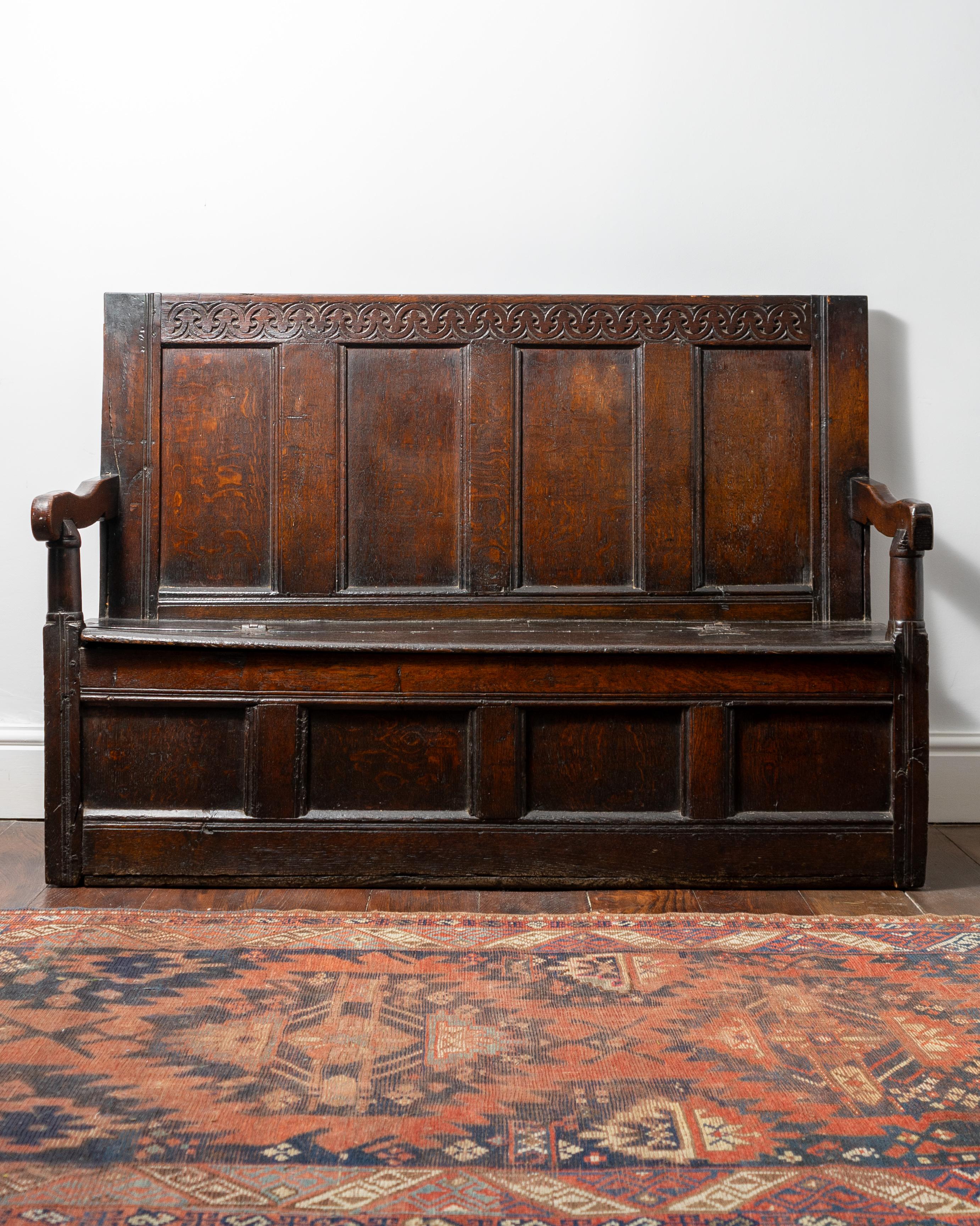 The quadruple-panelled back with stylized fleur-de-lys carved top-rail, the downswept open-arms on column-turned front supports, embracing a hinged boarded seat, over a quadruple-panelled front.

Provenance 
The Collection of Dr and Mrs Chris