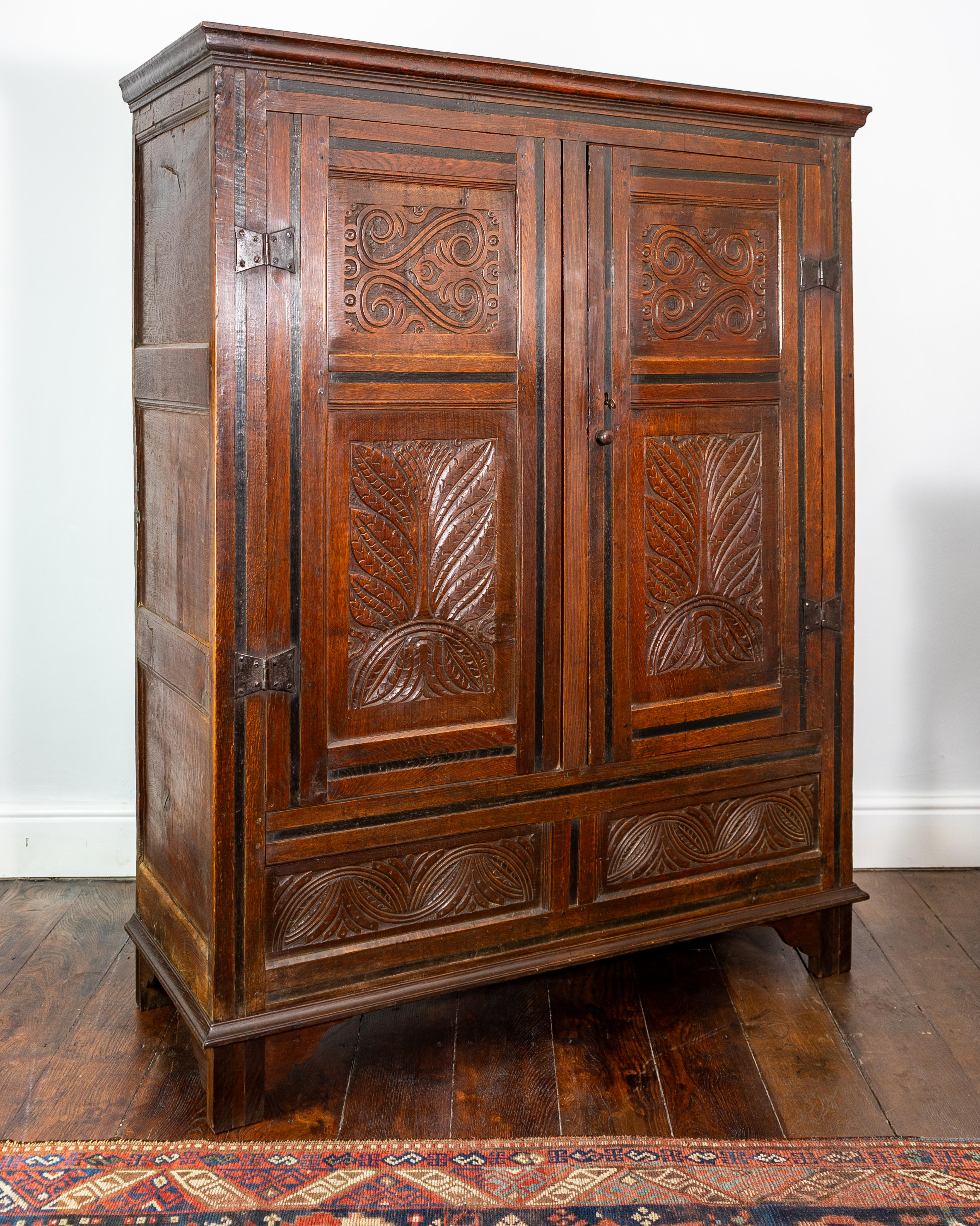 The panelled cabinet with two cupboard doors featuring double S-scroll carved panels, below further carved panels with large lunettes and stylised leafage, with original iron butterfly hinges flanking either side, stained black flat run-moulded