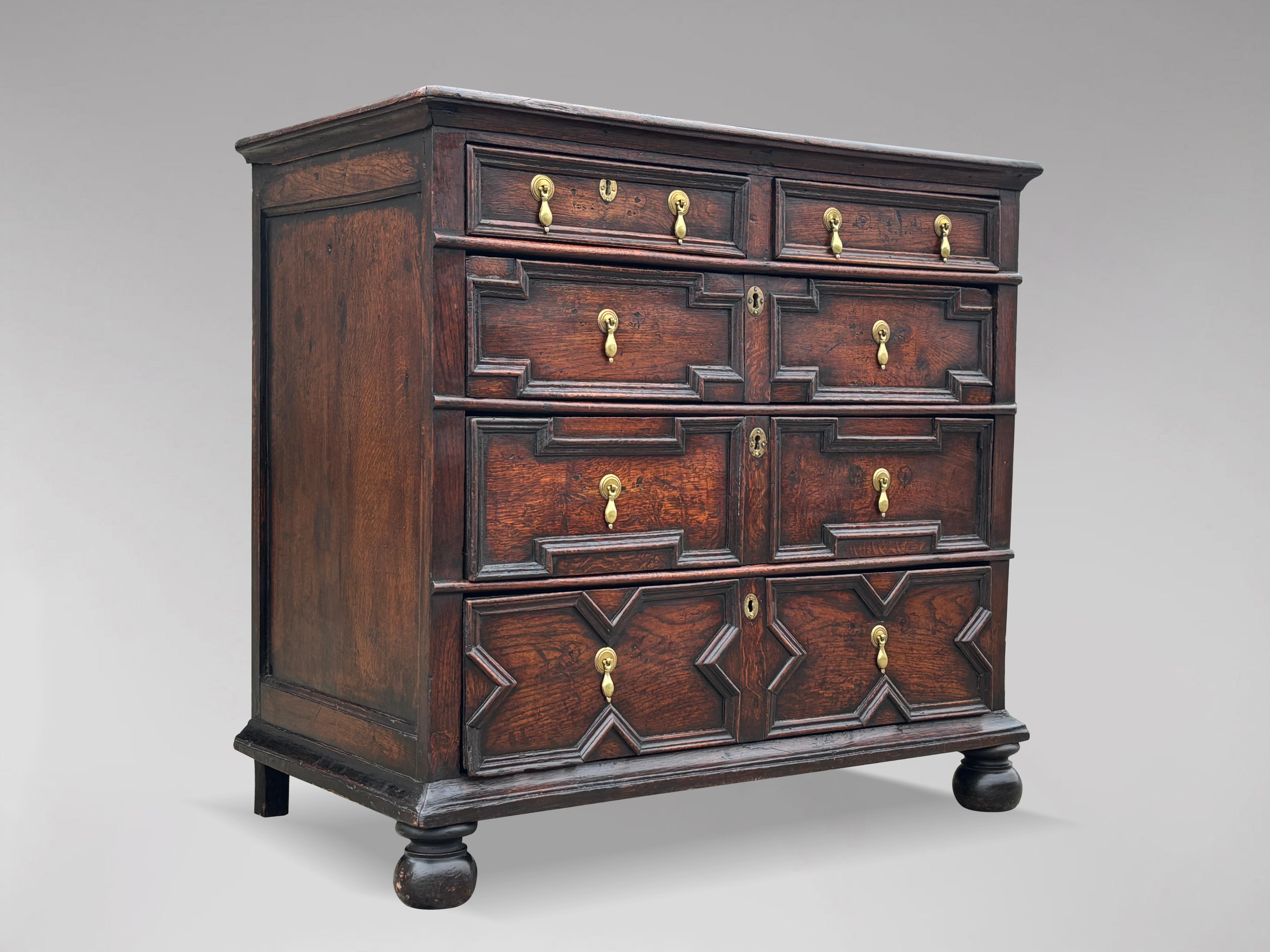 A 17th century, Charles II, Jacobean oak geometric chest of drawers of great colour & patina. Rectangular planked top with moulded edge above two small and three long graduated oak lined geometric moulded drawers with brass drop handles, escutcheons