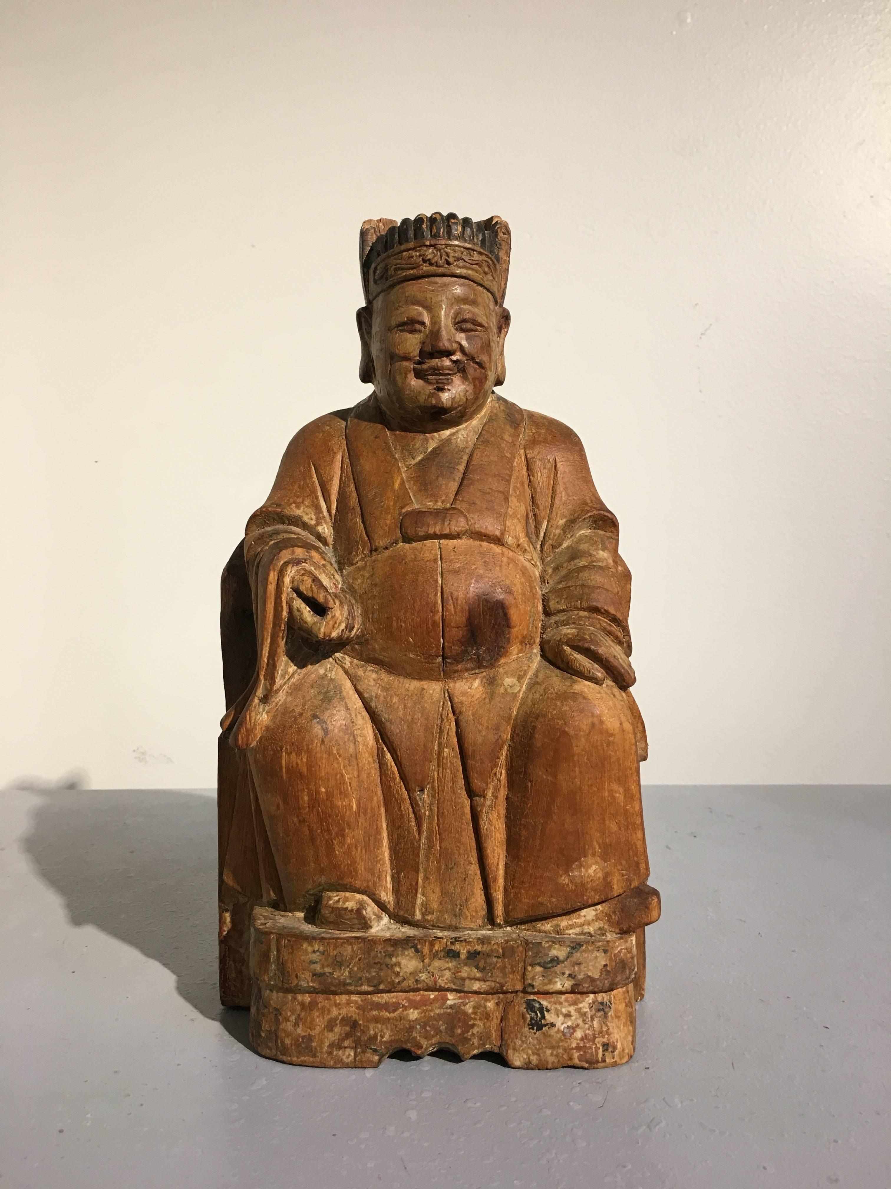 A charming late Ming dynasty Chinese carved camphor wood figure of the God of Wealth, named Caishen, mid-17th century. 
Carved from a single block of still fragrant camphor wood, Caishen, the god of wealth and prosperity, is portrayed seated upon a