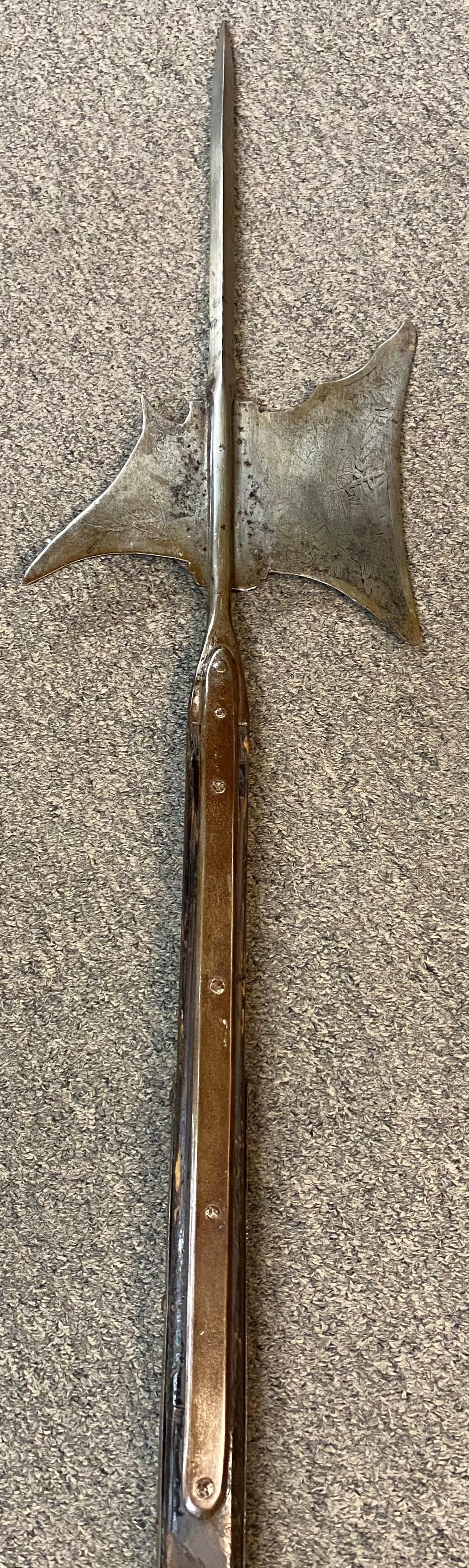 A fine example of a mid-17th century steel halberd with pole arm, with a diamond shape thrusting point, axe blade with shallow concave cutting edge featuring overall etched decoration, slightly curved rear fluke with downward-pointing beak that is