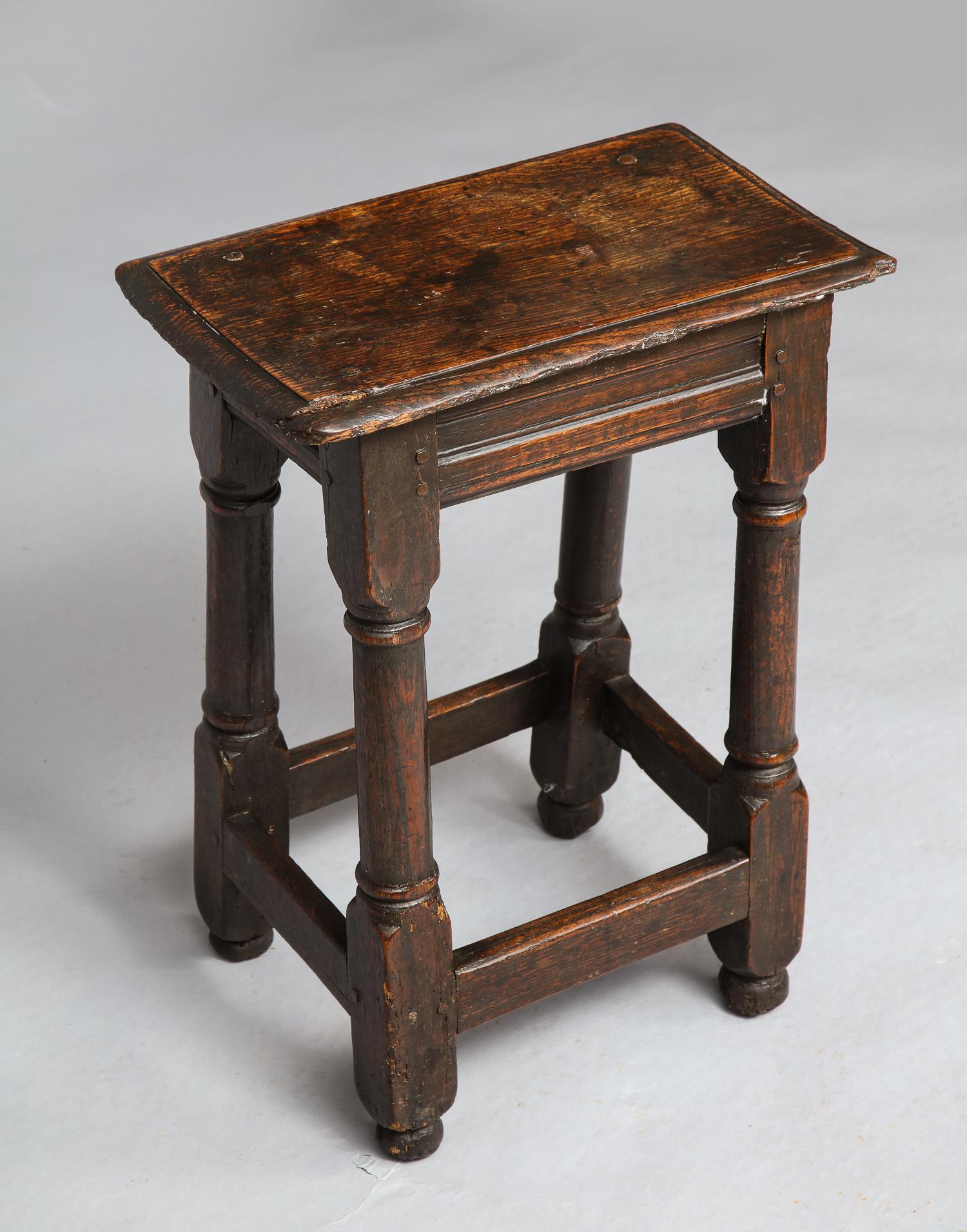 Fine mid-17th century English oak joint stool, having a single plank thumb molded top over channel molded aprons, standing on slightly splayed balustrade turned legs joined by box stretcher and standing on original ball feet, the whole possessing