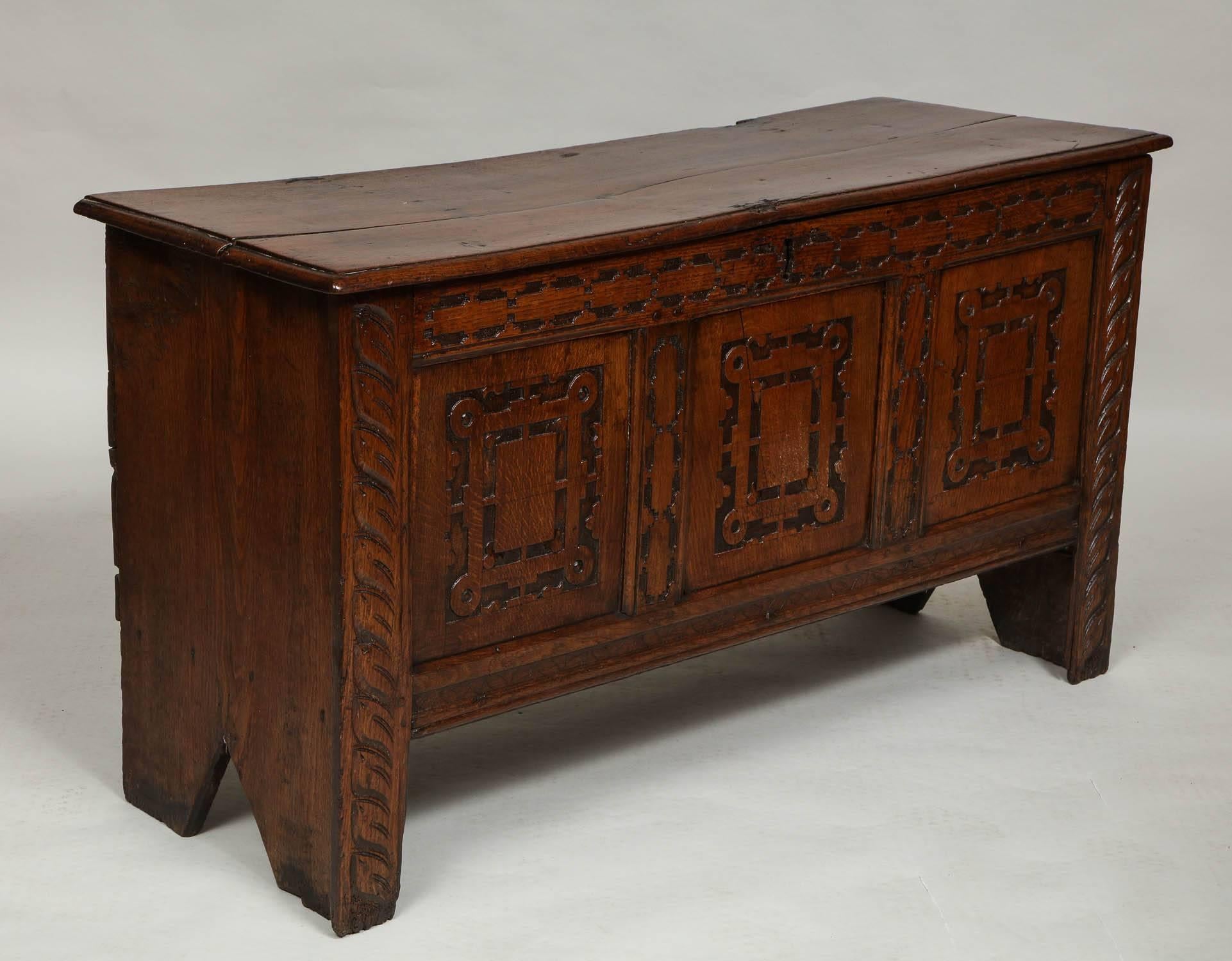 Fine 17th century English oak coffer, the two plank top with thumb molded edge over slab sides with bootjack feet, the front of panelled construction having geometric carved panels and rails, the stiles with foliate details, retaining 18th century