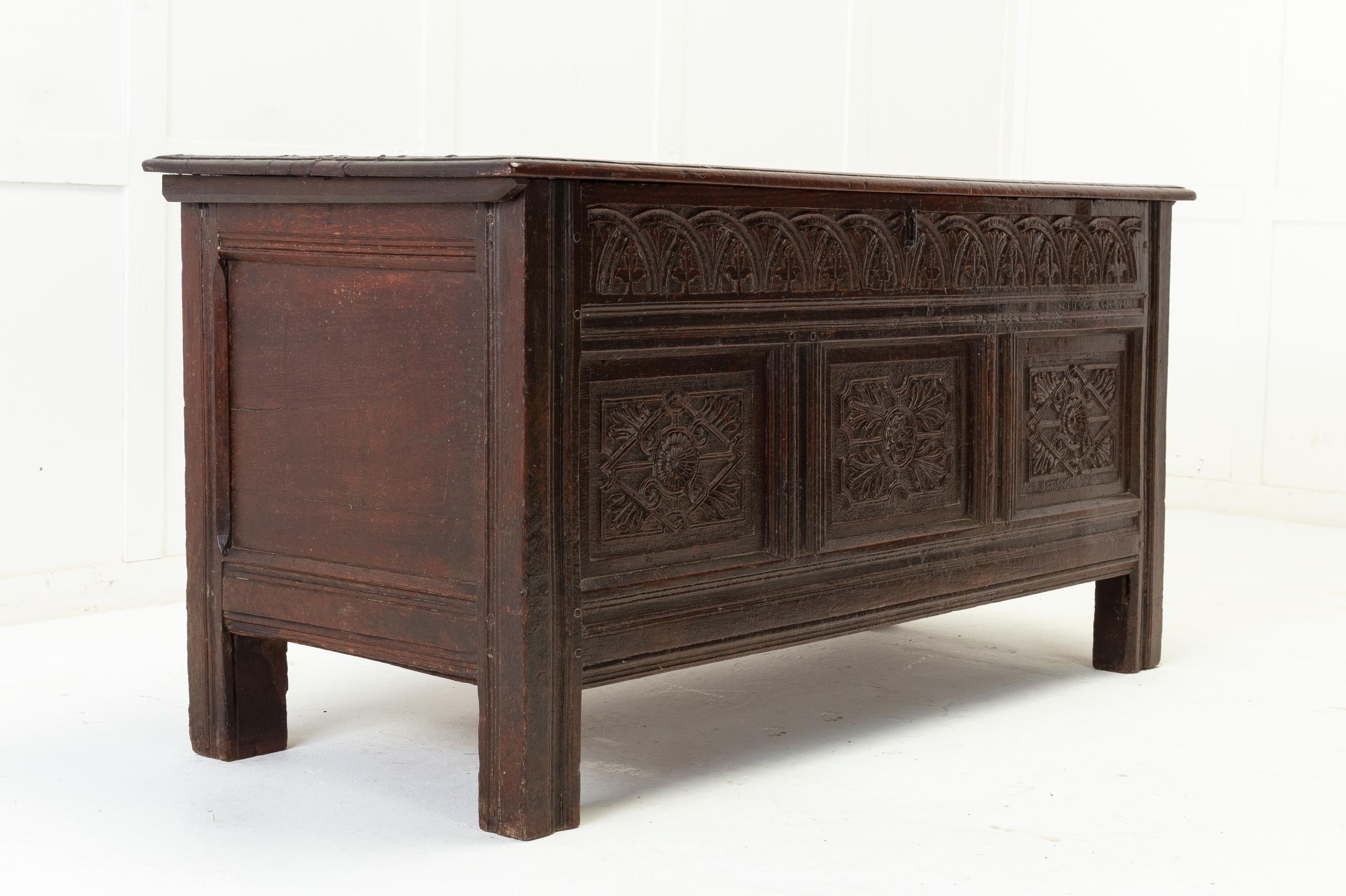 17th century English oak panelled coffer. Having a two plank top with iron hinges. Inside has a small boxed compartment. The frieze and front panels are generously carved with detailing such as rosettes, foliage and acorn leaves. Panelled sides and