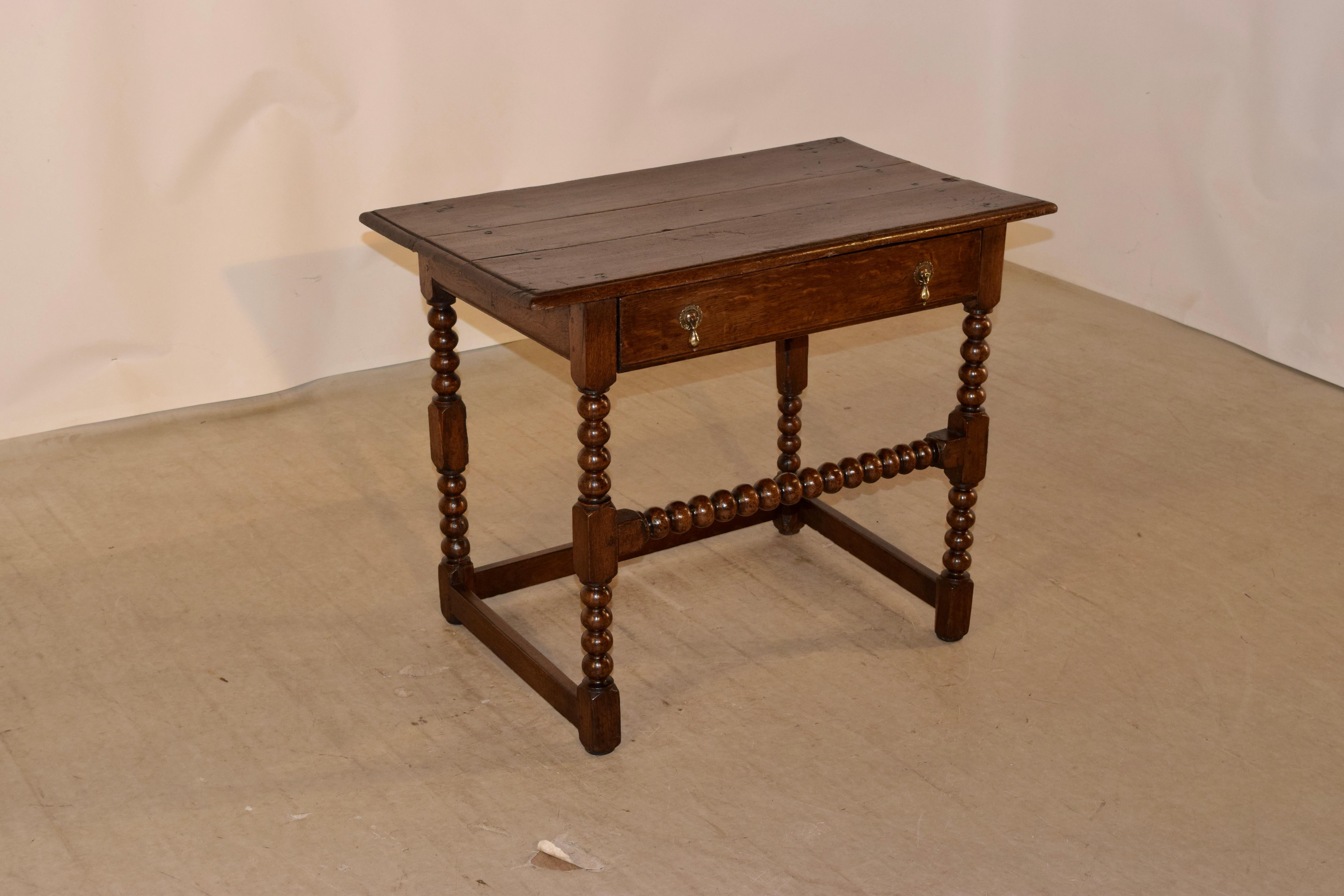 17th century oak side table from England with a beveled edge around the top, which has hand pegged construction. The apron is simple and contains a single drawer over hand turned bobbin legs, joined by a matching stretcher in the front, and simple