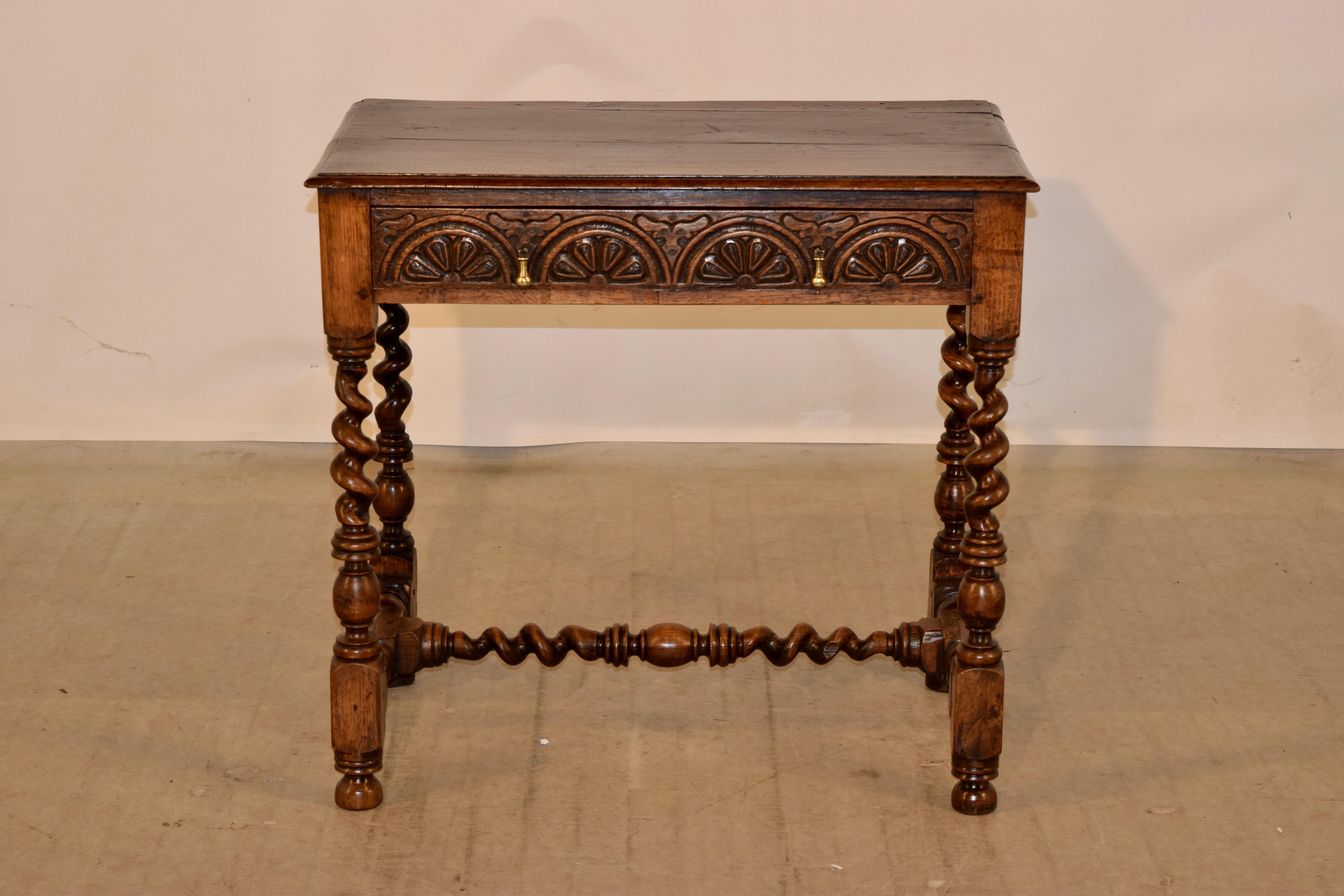 17th century oak side table from England with a plank top which has a beveled edge, following down to simple sides and containing a single drawer in the front. The drawer front is hand-carved decorated and has hand cast drop pulls. The table is