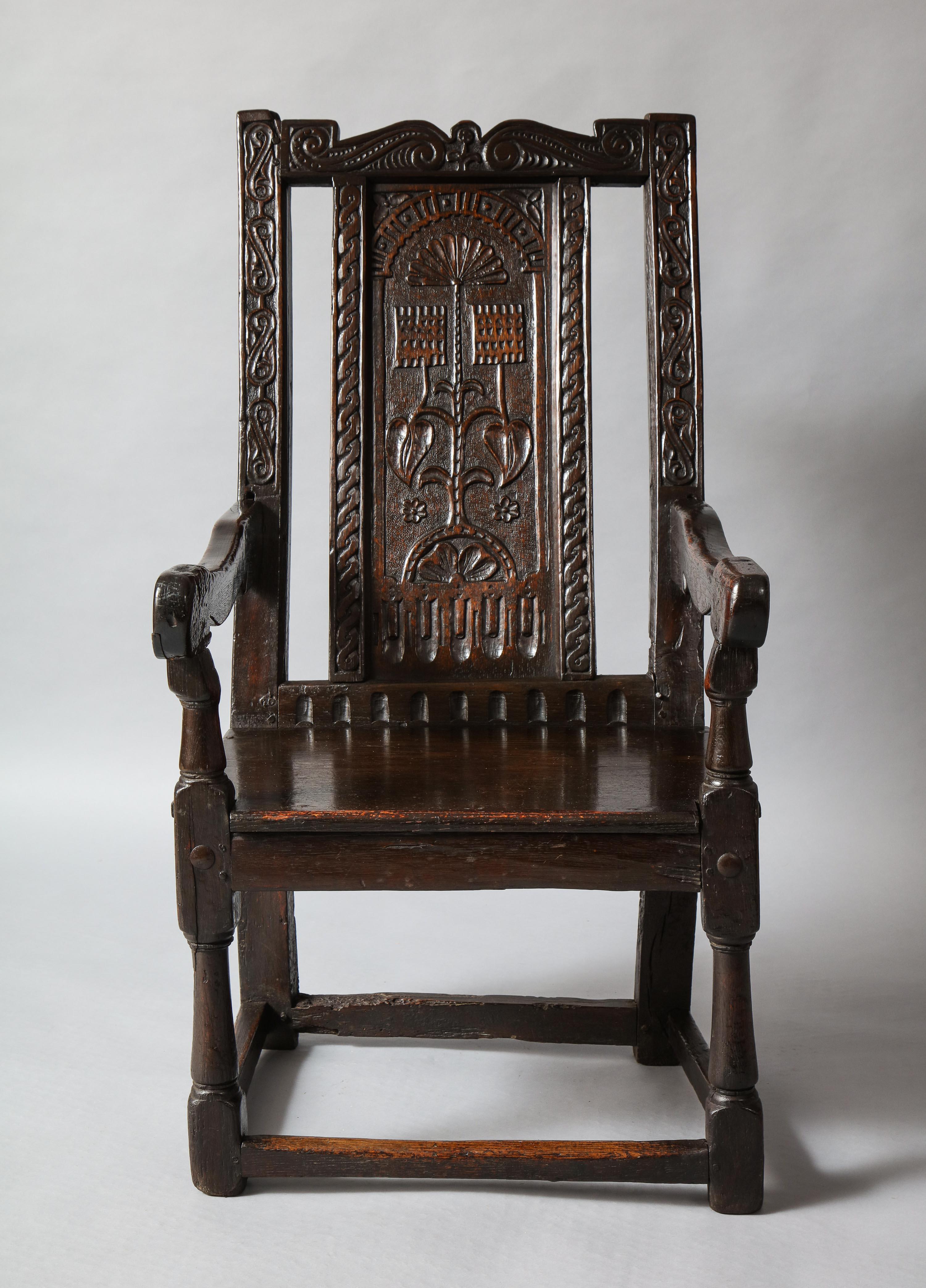 Most unusual 17th century English or welsh wainscot chair having a shaped and scroll carved crest over similarly carved rails, the central panel with fan shell and square foliate design, having shaped arms and turned supports and legs, the whole
