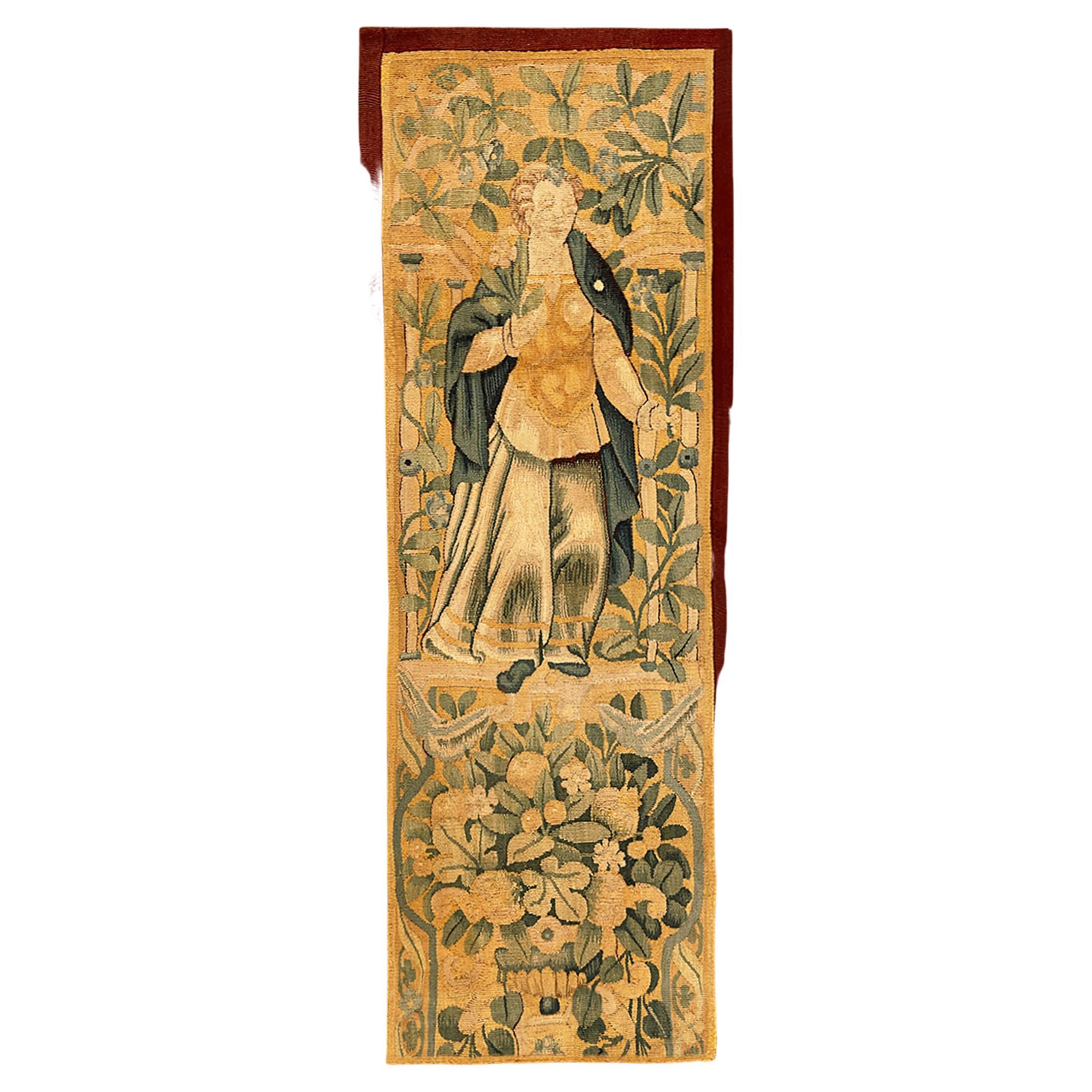 A 17th century Flemish Historical Tapestry panel. This vertically oriented decorative tapestry panel depicts a regal female figure at top, with a floral reserve below her. The central area is enclosed within a narrow monochrome border. Wool with