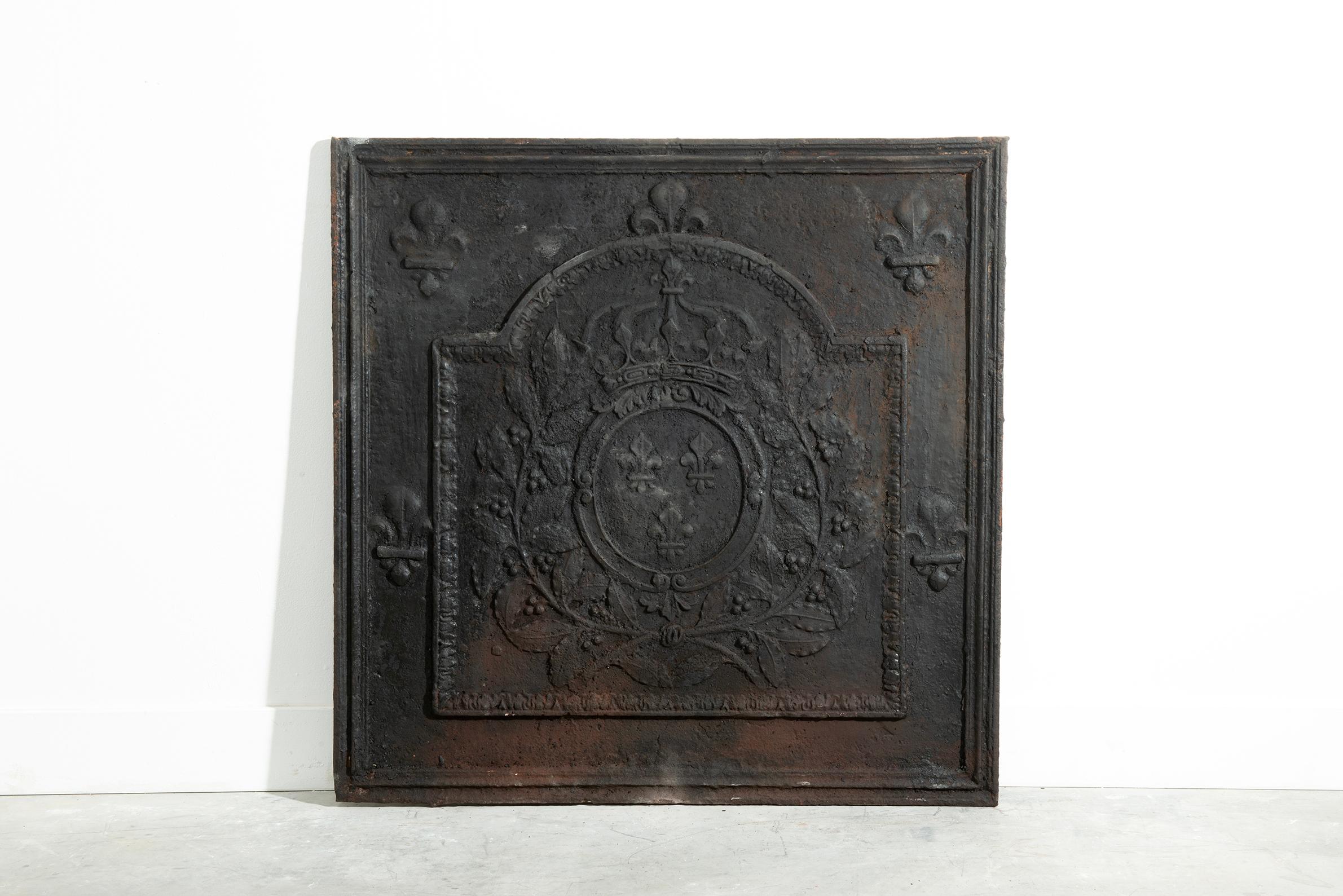 Questo imponente parafuoco antico in ghisa proveniente dalla Francia, risalente al XVII secolo, presenta lo stemma reale di Francia con tre gigli sotto una grande corona, circondata da rami di alloro e incorniciata da ulteriori motivi a giglio in