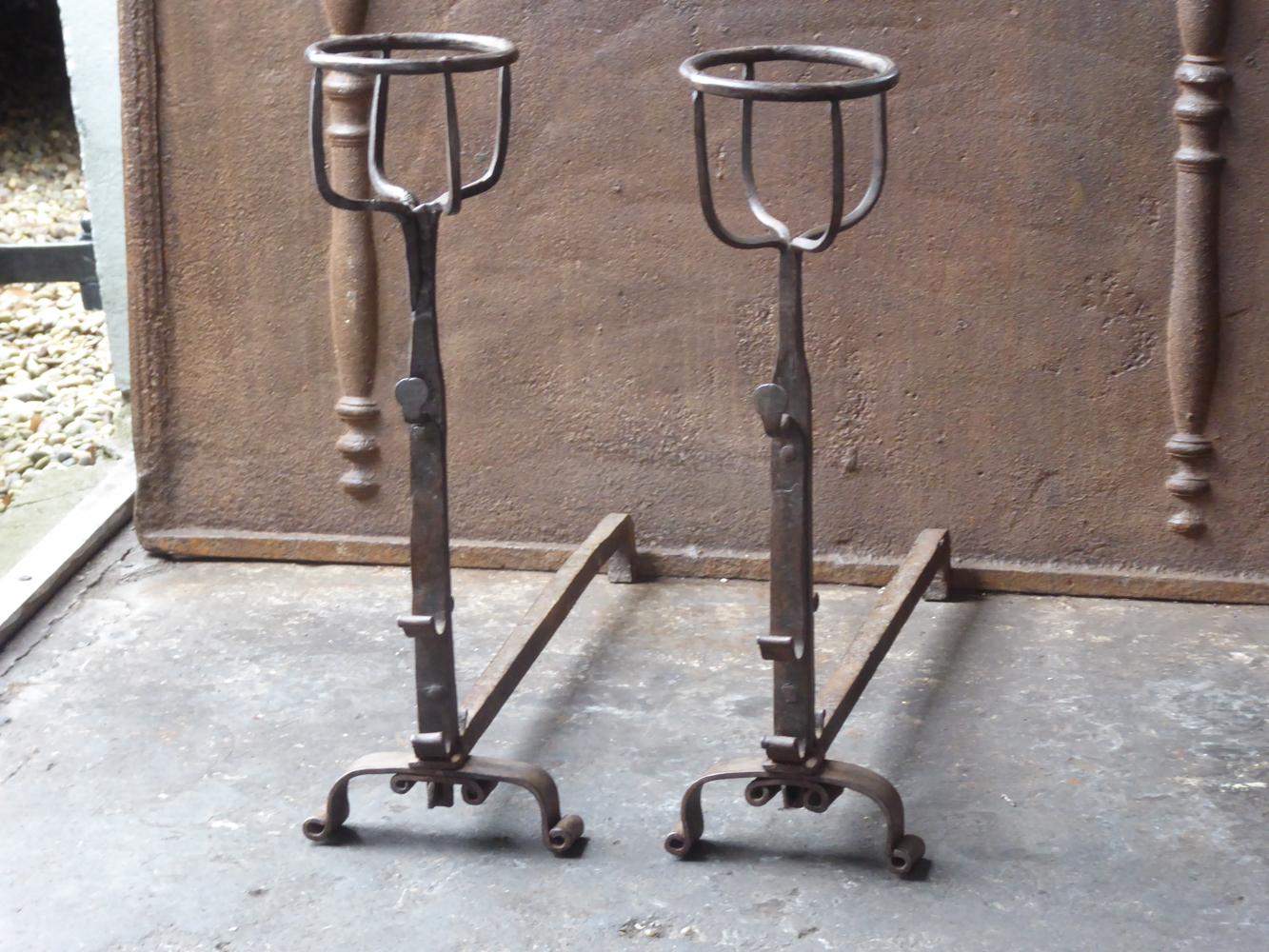 17th century French andirons made of wrought iron. The style of the andirons is Gothic. The andirons have spit hooks to grill food. They have a natural brown patina. The condition is good.