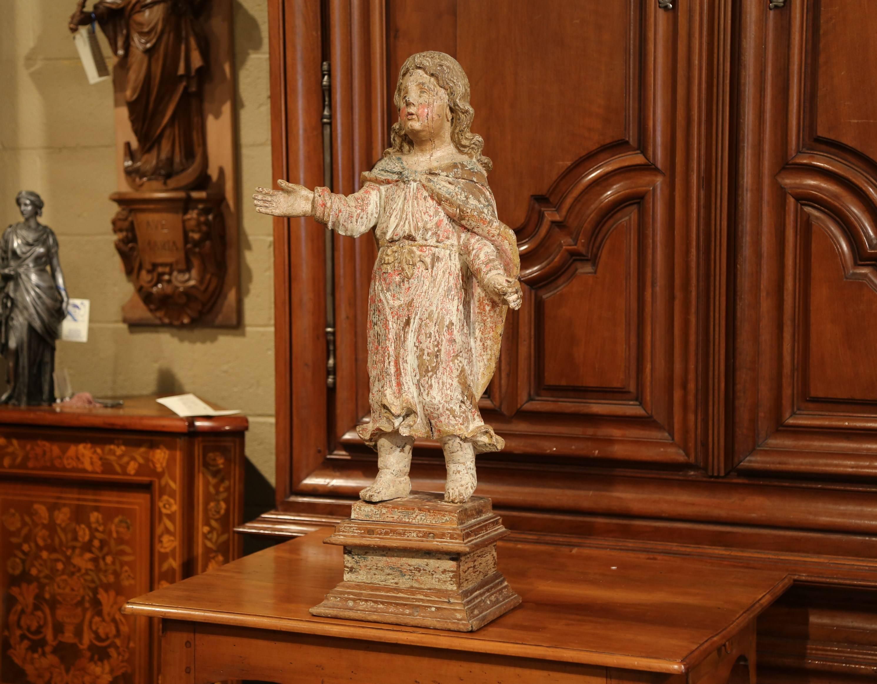 This exquisite, antique figure was carved in Southern France, circa 1650. Standing on a square walnut base, the detailed statue features a young child with long hair with a right hand up. The young adult is wearing a traditional tunic with a
