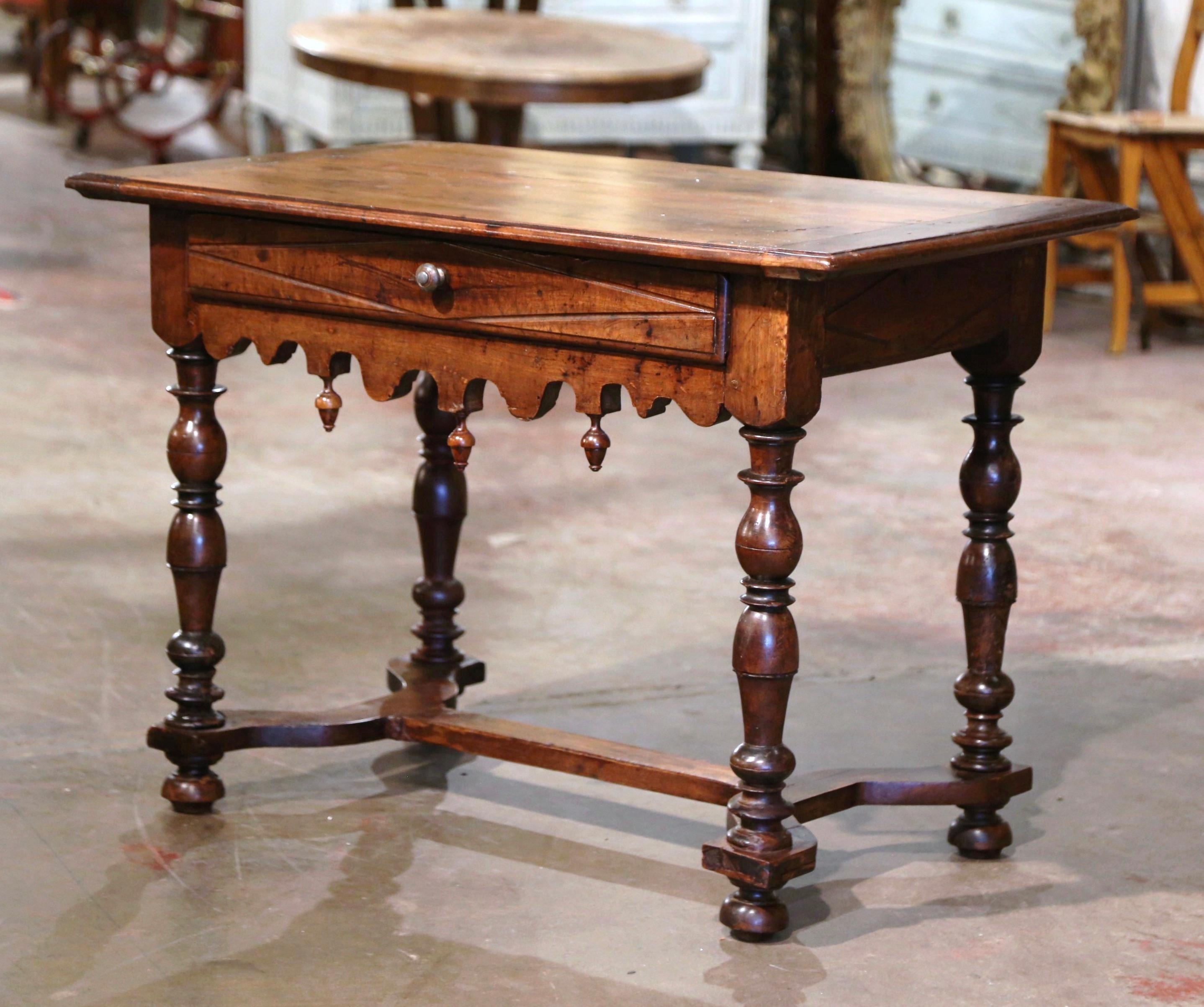 Crafted in the Perigord region of France, circa 1670, the antique table stands on four thick carved turned legs ending with bun feet, and embellished with an elegant curved stretcher at the base. The side table features a large drawer across the