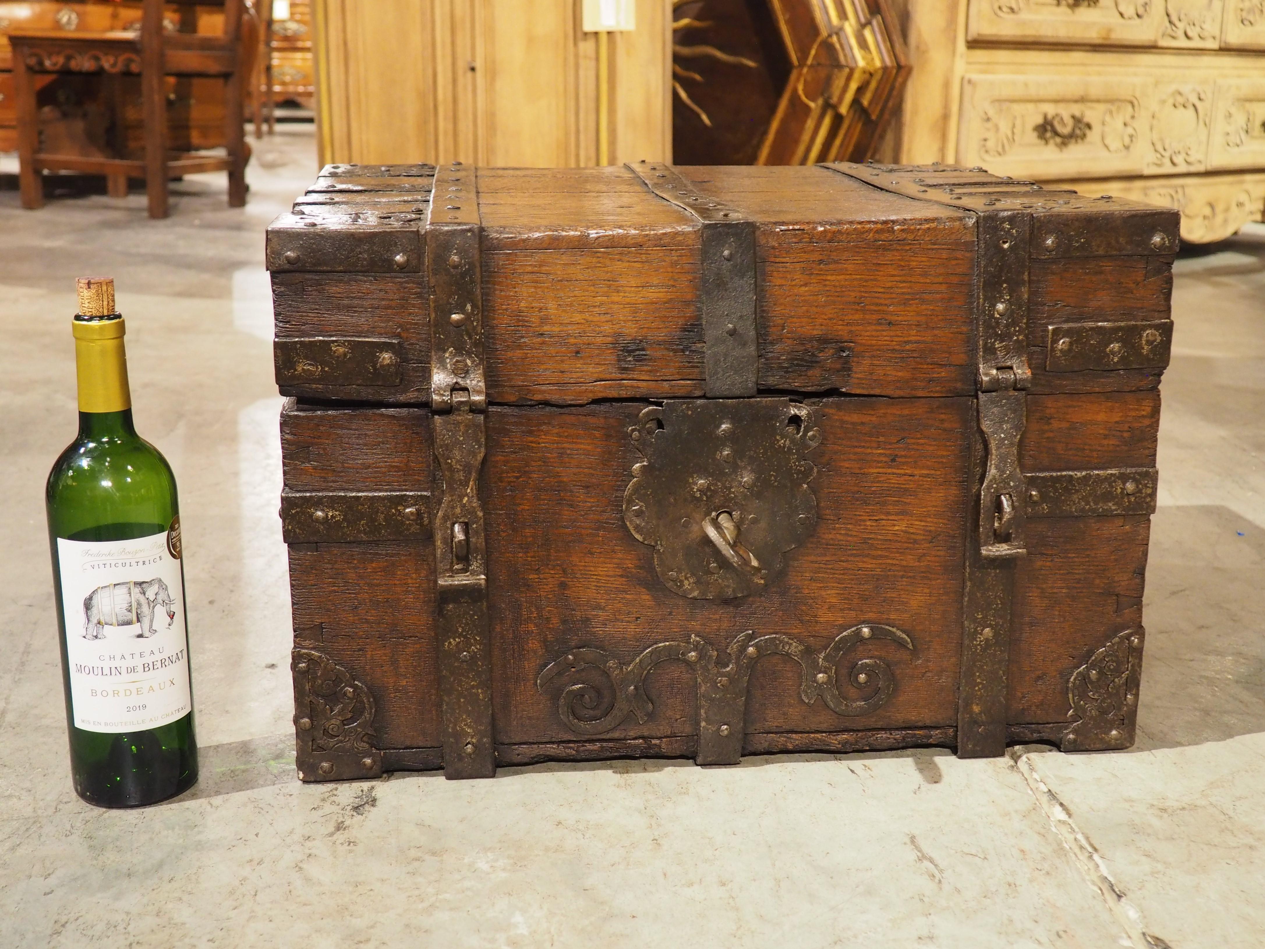 Ornato da un impressionante reticolo di cinghie, questo salvadanaio in quercia e ferro proveniente dalla Francia del XVII secolo è funzionale ed esteticamente accattivante. In ogni angolo del coperchio si trova un elaborato e stilizzato fiore di