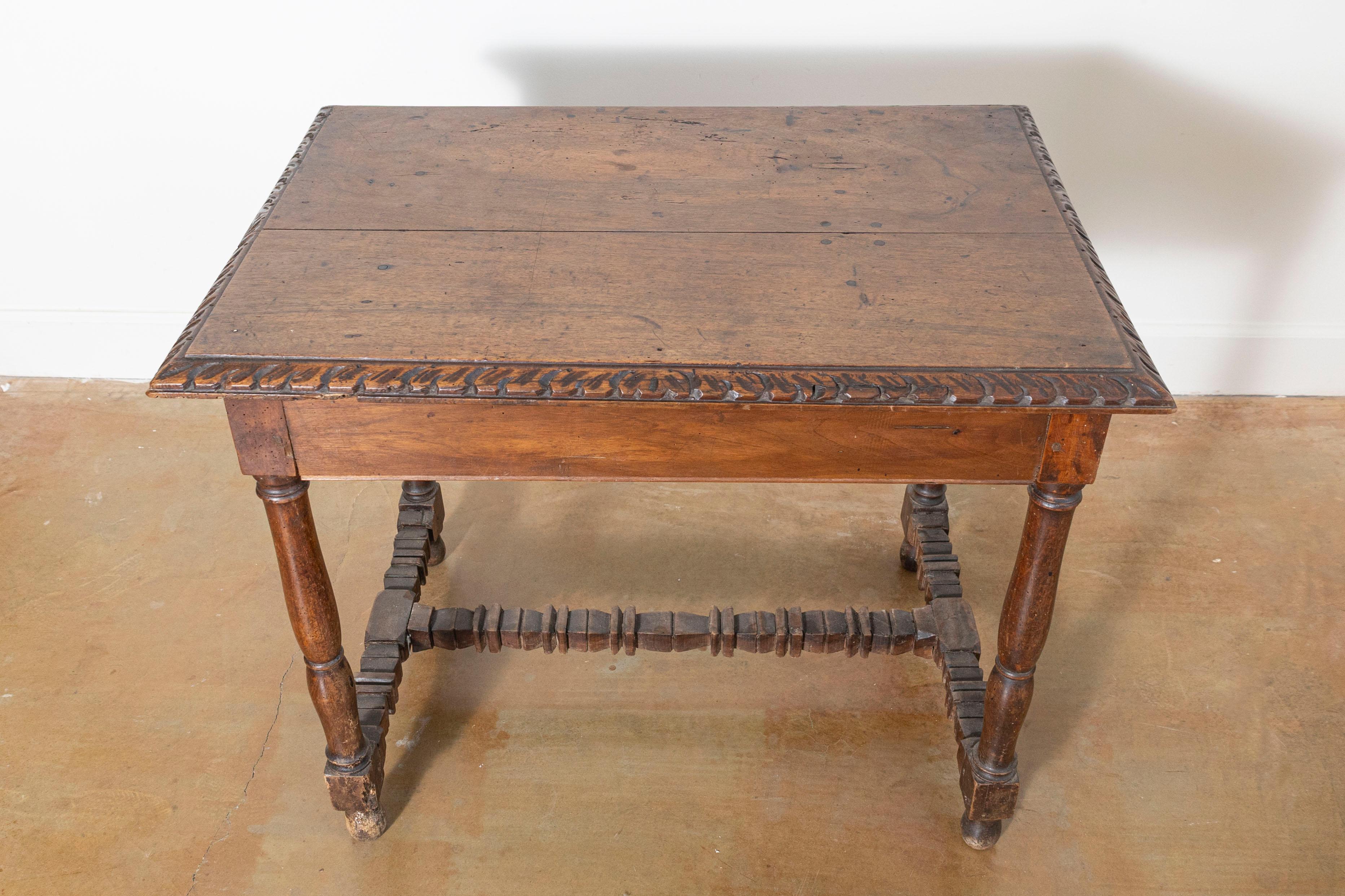 Cette table d'appoint française du XVIIe siècle est un exemple étonnant d'artisanat ancien et de design intemporel. Fabriquée en noyer massif, la table présente un plateau rectangulaire avec un tablier magnifiquement sculpté à la main et orné de