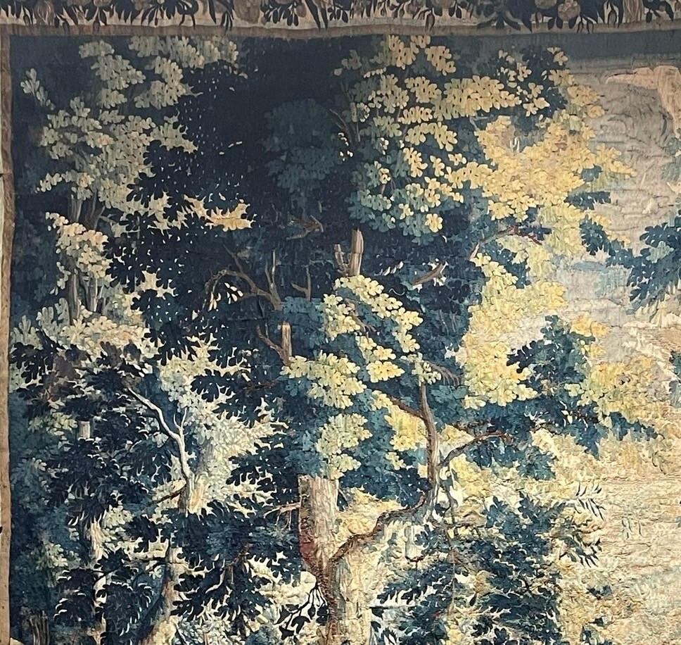 This exquisite 17th-century French Verdure tapestry captures the essence of pastoral beauty with its meticulously hand-woven wool intricacies. Measuring [dimensions], it transports viewers to lush landscapes teeming with verdant foliage, majestic