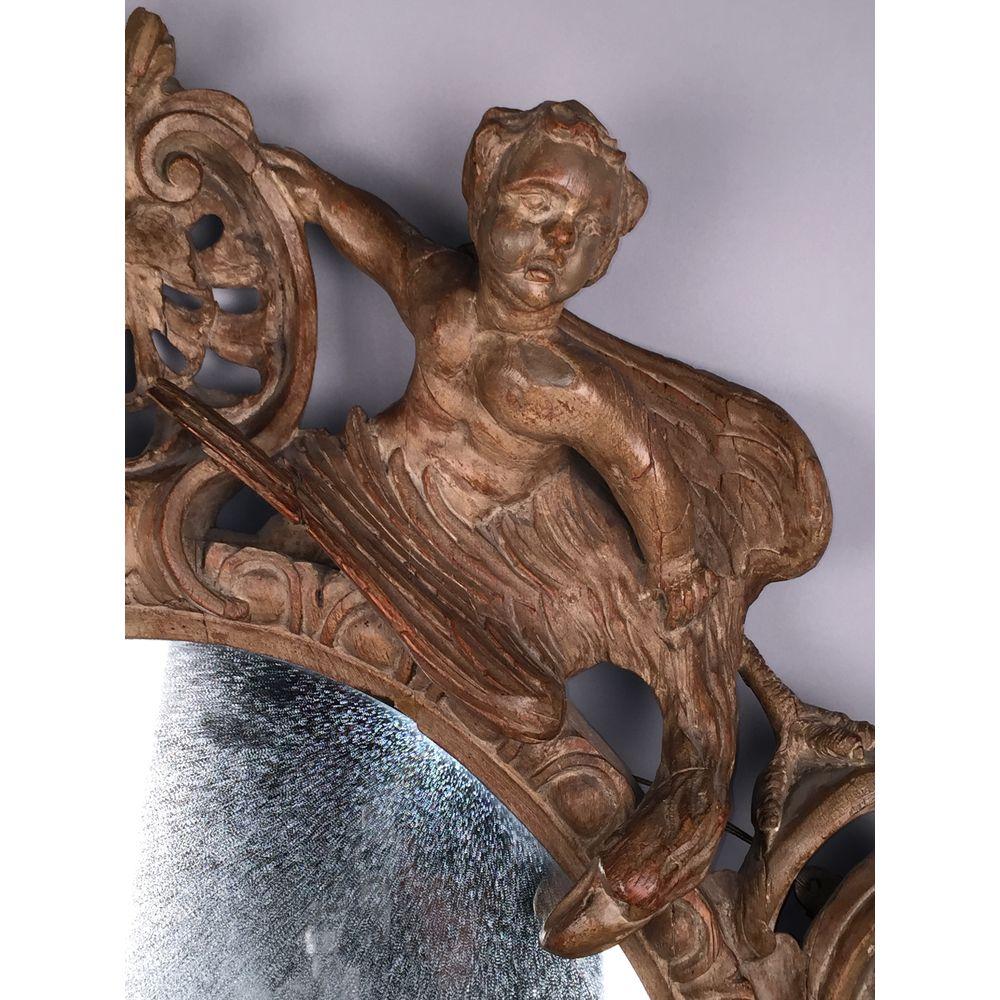 Un rare miroir ovale sculpté de style baroque allemand (Barock).
Début du XVIIe siècle, vers 1620-1630.

Le cadre est superbement sculpté. L'écusson est orné de deux chérubins soutenant un cartouche, assis sur des aigles en représentation.
La base