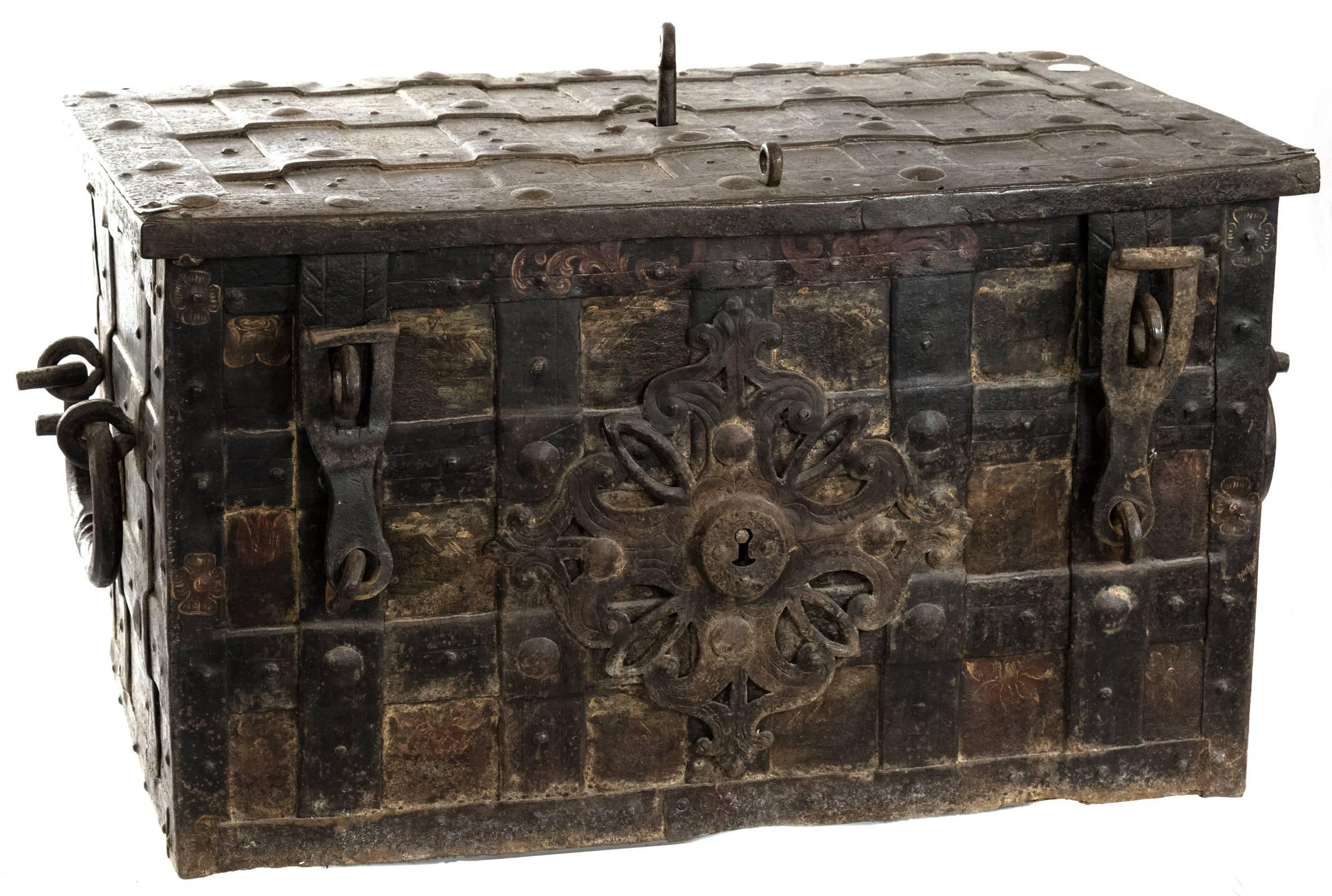 An iron chest of rectangular form bound in studded iron straps around decoratively painted floral panels, the centred top lock with key shooting bolts. The front having two hasps with padlocks and a pierced quatrefoil escutcheon with engraved