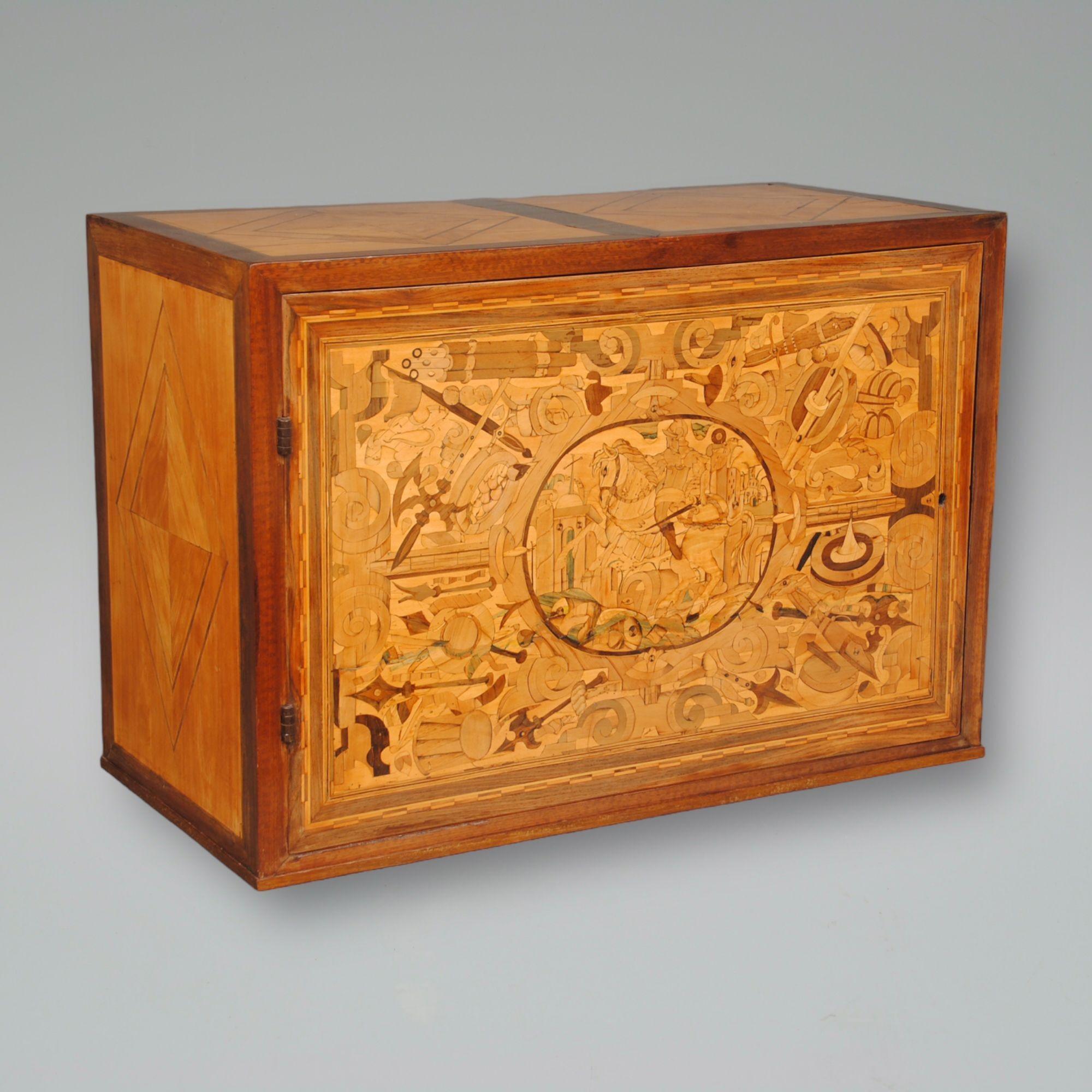 A German single door table cabinet. The front is inlaid with a Knight on horse back set within an oval and surrounded with a trophy of arms. The fitted interior with drawers and cupboards which are finely inlaid with architectural scenes. Retaining