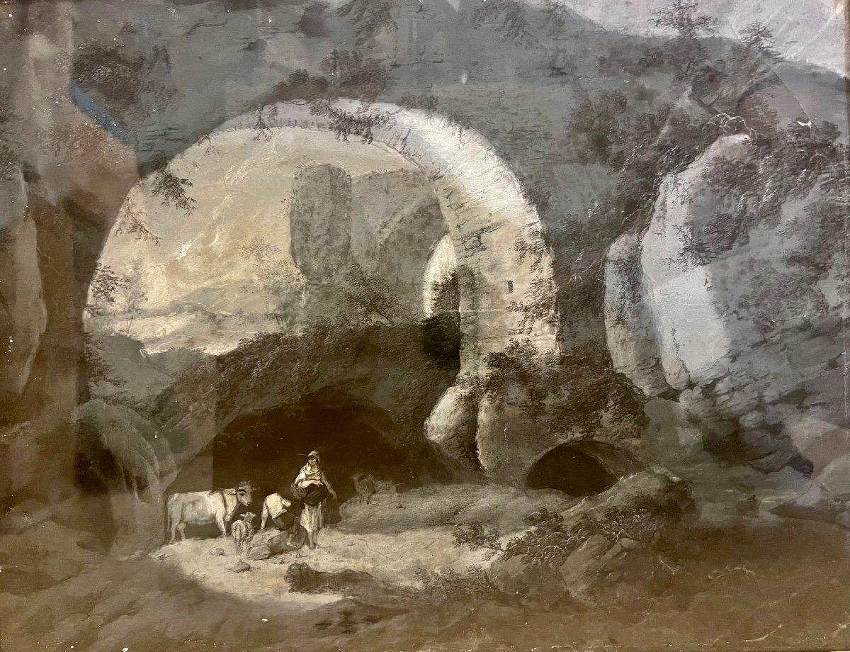 Nous vous présentons cette œuvre d'art au pastel gris extrêmement ancienne qui capture une scène pastorale tranquille représentant deux bergers guidant leur bétail sous la grande arche d'un imposant pont romain. Le dos du tableau révèle une