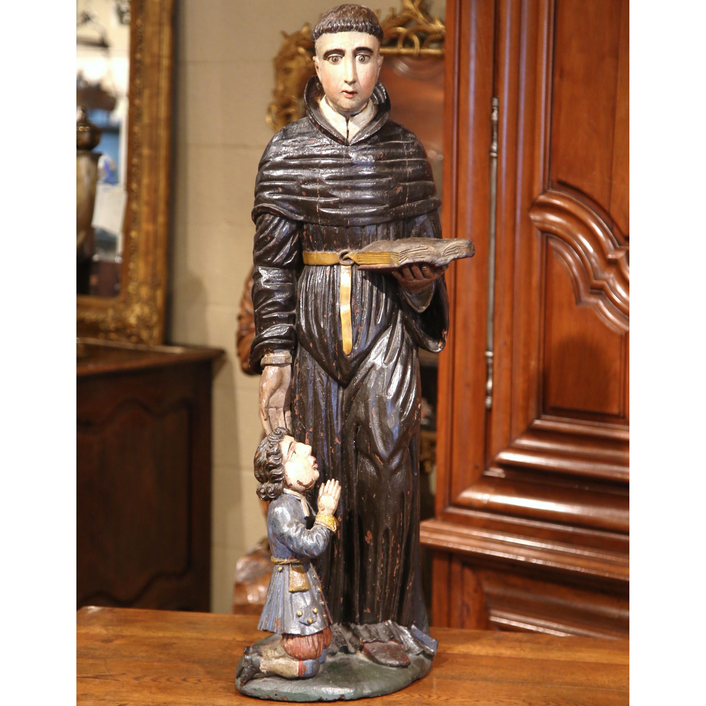 Esta gran estatua antigua de madera policromada de San Nicolás de Tolentino con un joven fue tallada en Italia, hacia 1680. La composición escultórica religiosa presenta al Santo vestido con la sotana tradicional; sostiene un libro teológico. Junto