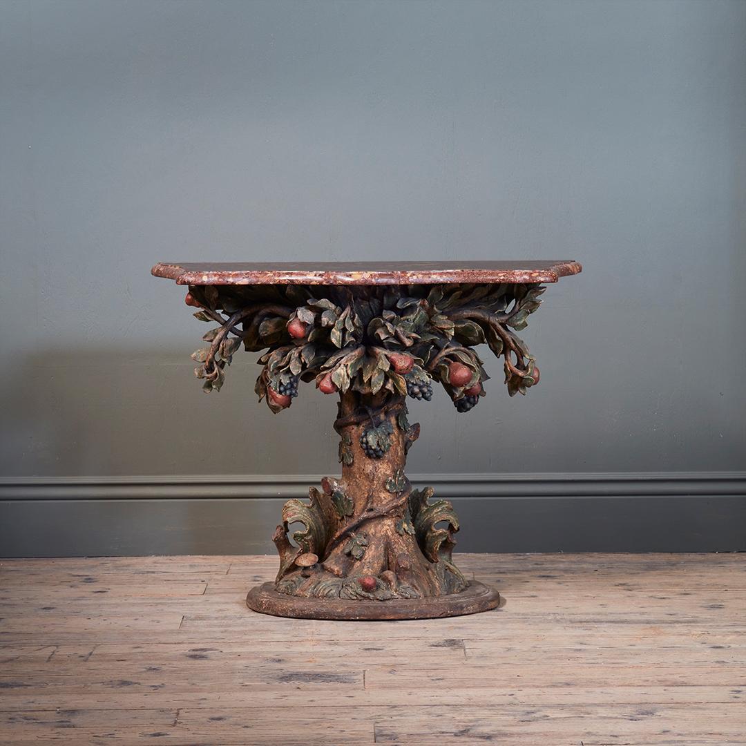 Scolpita con un eccezionale effetto naturalistico, la base di questa consolle ha la forma di un albero di pere intrecciato con viti, con le radici ben piantate in una collinetta erbosa, ricca di vegetazione. Con piano in marmo Breccia Capitolina