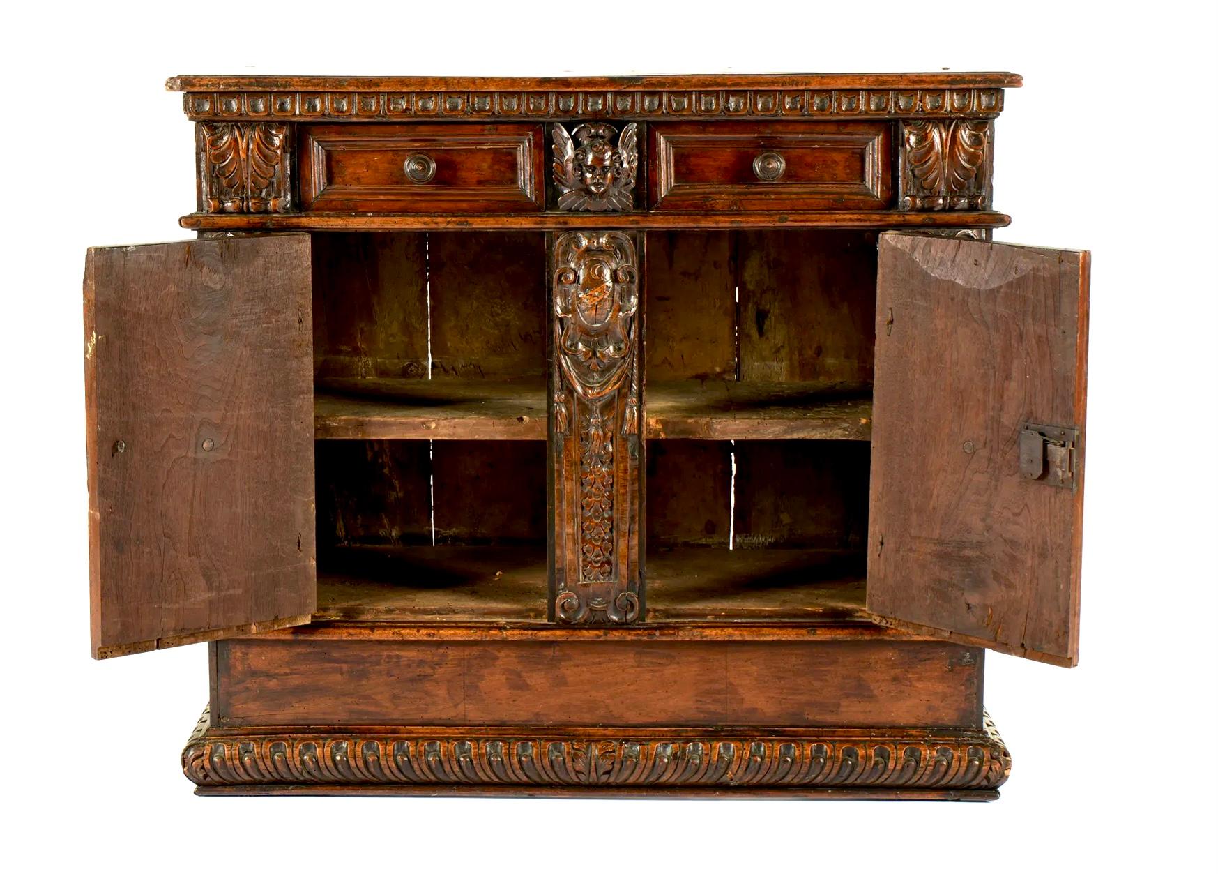 Credenza italiana de nogal tallado del siglo XVII. La credenza está bellamente elaborada con un intrincado trabajo en madera con tallas decorativas de criaturas mitológicas y follaje a lo largo de las puertas, cajones y laterales. La madera de nogal