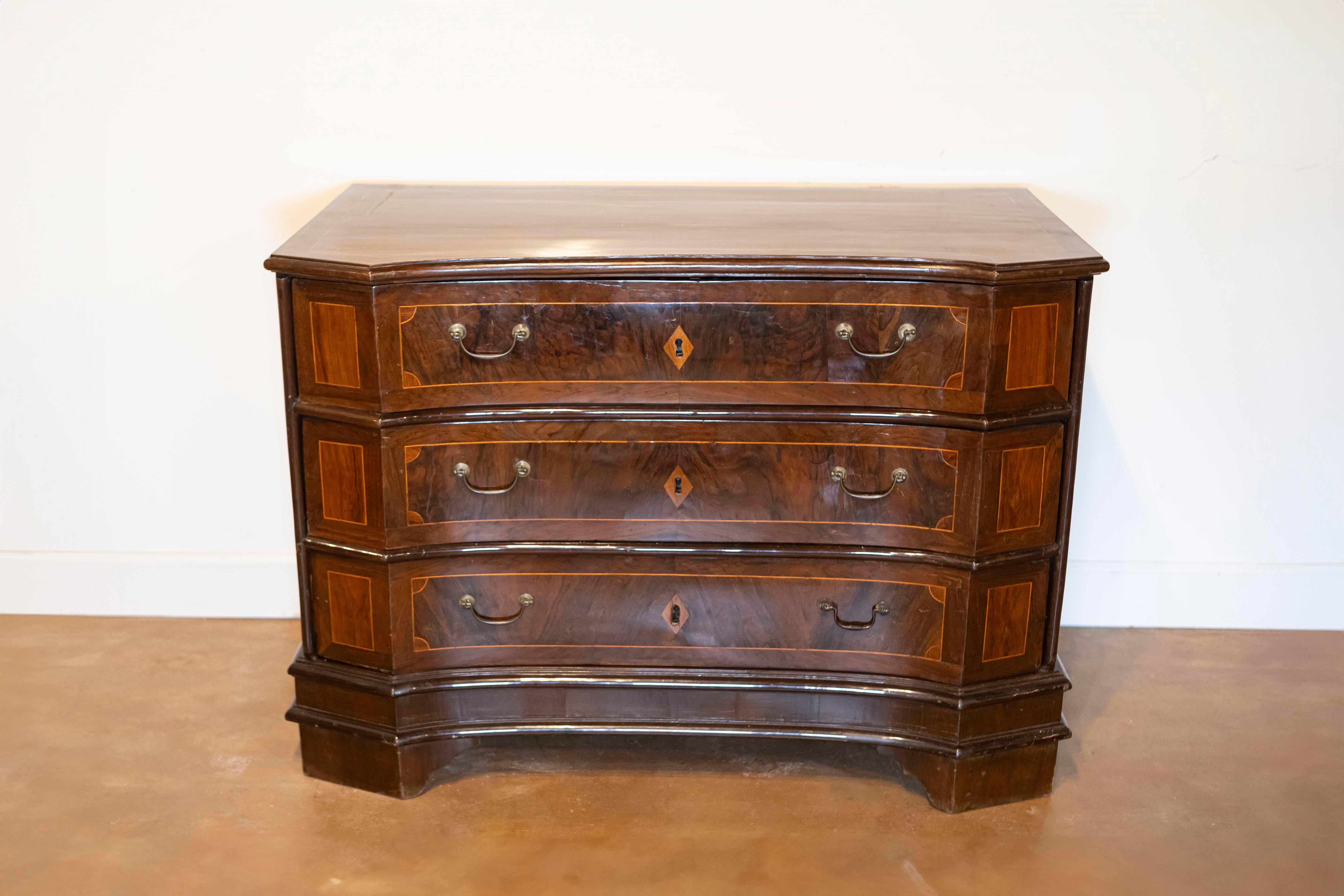 This 17th-century Italian commode is an exquisite example of Baroque design, characterized by its bold form, intricate details, and refined craftsmanship. The commode features a serpentine front, with three spacious drawers that gently curve