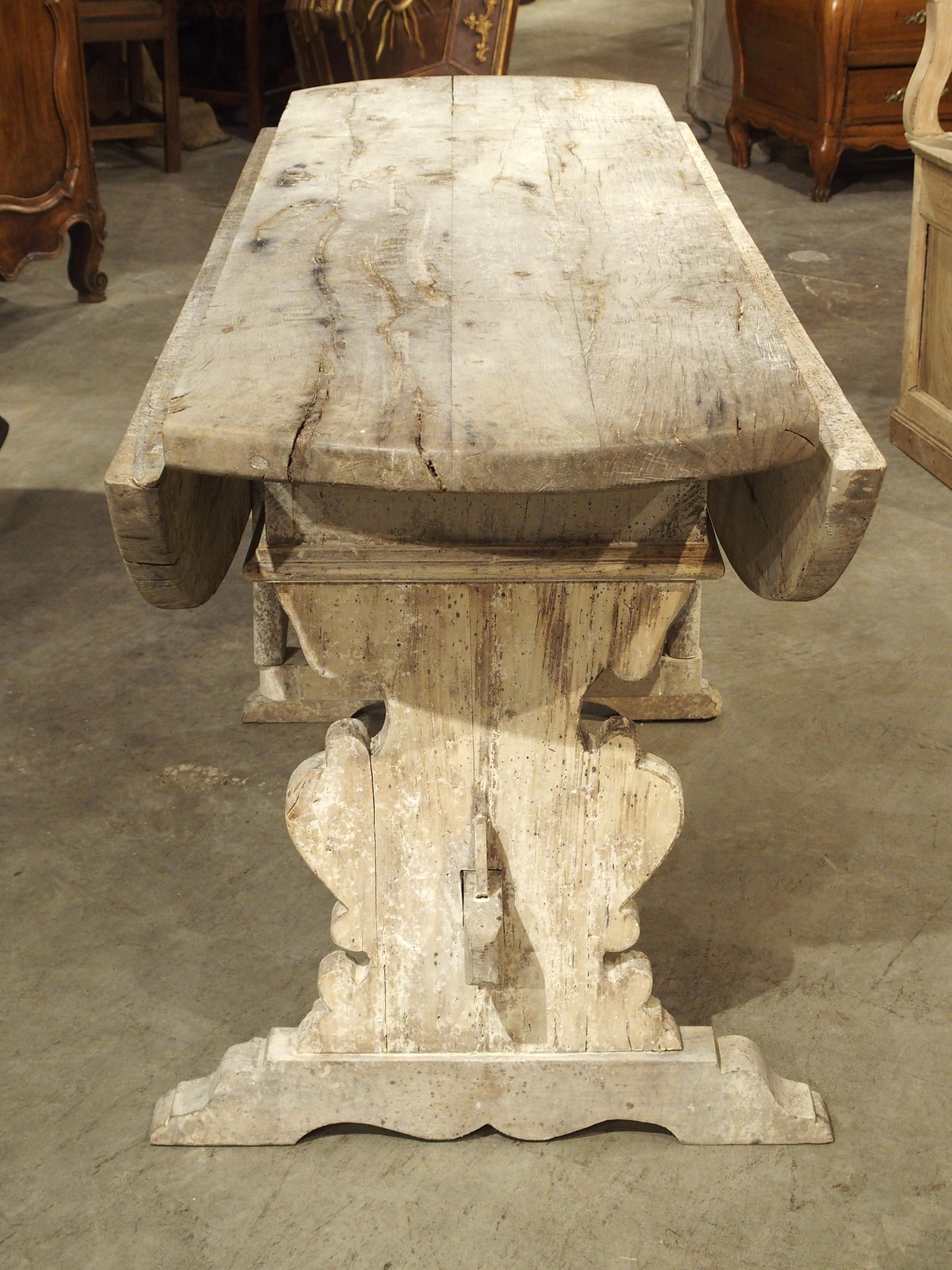 A wonderful and unique piece of furnishing from Italy, this oval drop-leaf table was hand-carved in the 1600s. The oak wood has since been whitewashed, giving the wood a white-gray hue with accents of cream, all while allowing some of the darker,