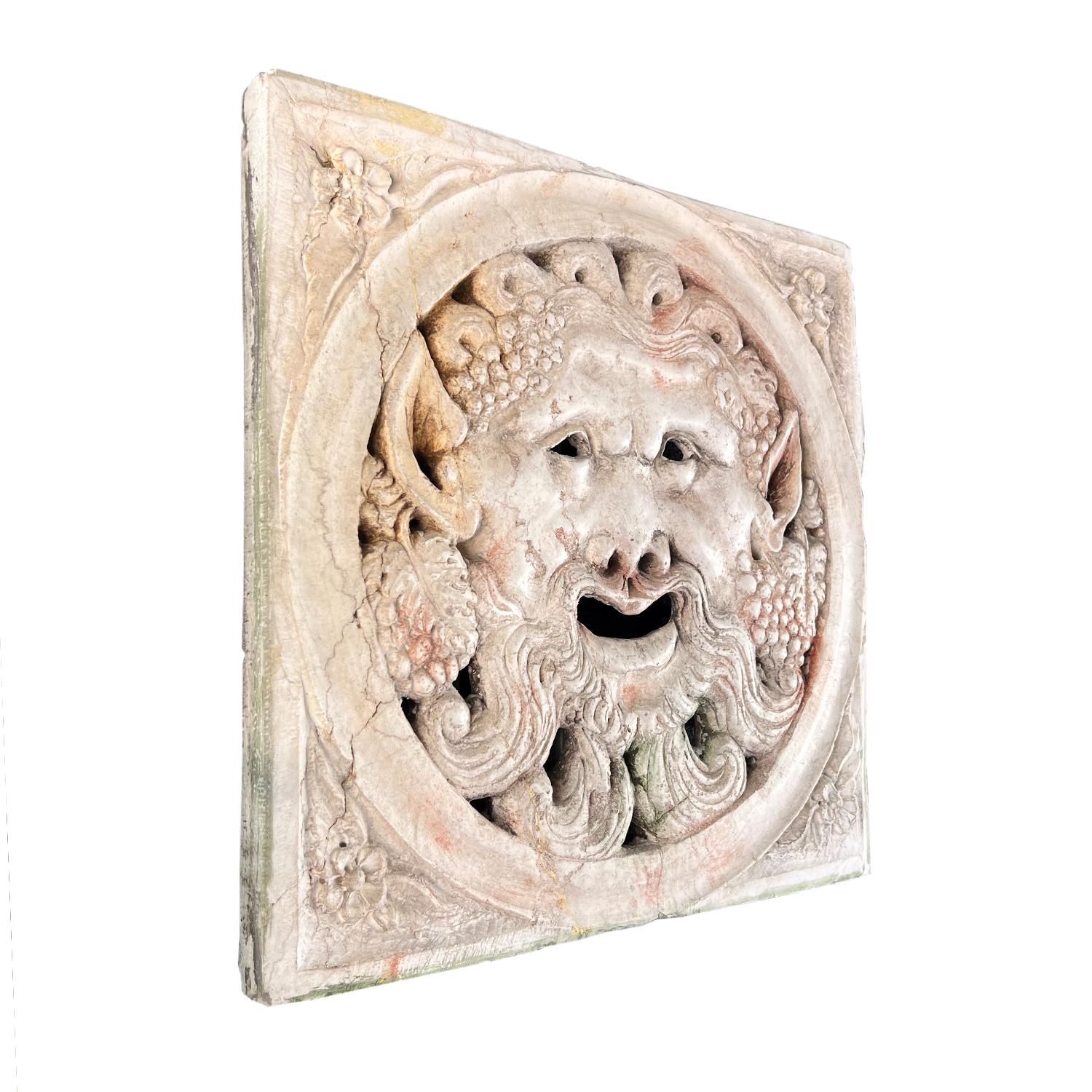 An antique Italian medieval square marble relief carved as a grotesque mask with big ears surrounded by grapes and leaves, in good condition. It was used in the Renaissance period as a mailbox cover. Minor fading, scratches due to age. Wear
