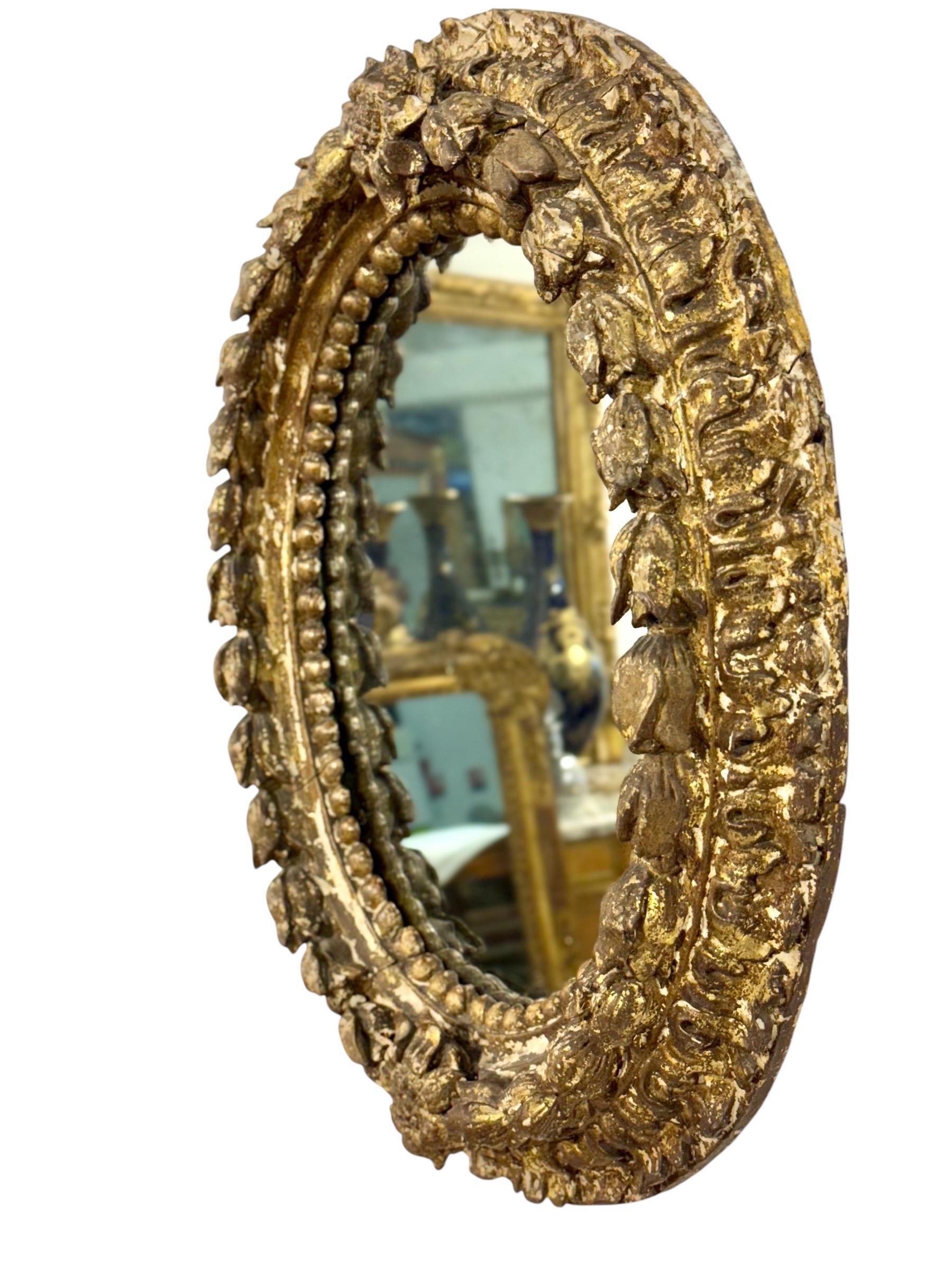 Cet exquis miroir ovale est une authentique pièce italienne datant du XVIIe siècle, richement sculptée dans le bois et finie avec sa dorure d'origine. Le cadre est orné d'une guirlande continue de fleurs et de feuillages, entrecoupée de perles