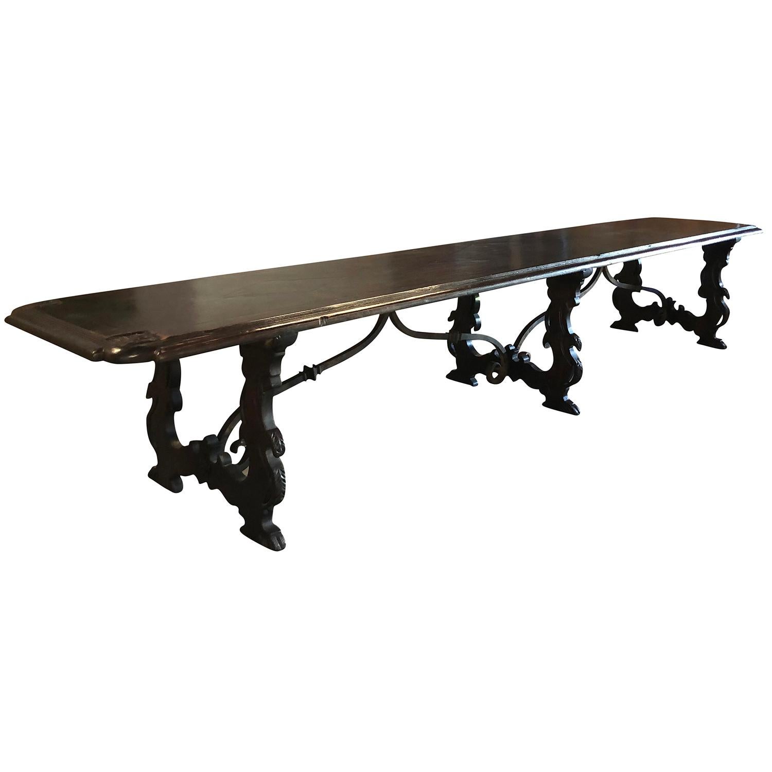 An important and oversized Tuscan Refectory table. The table top was carved by hand in a single dark Walnut plank and is adorned with carved Fleur de Lys on each corner. The top is raised on shaped trestle ends and is joined by an iron trestle base.