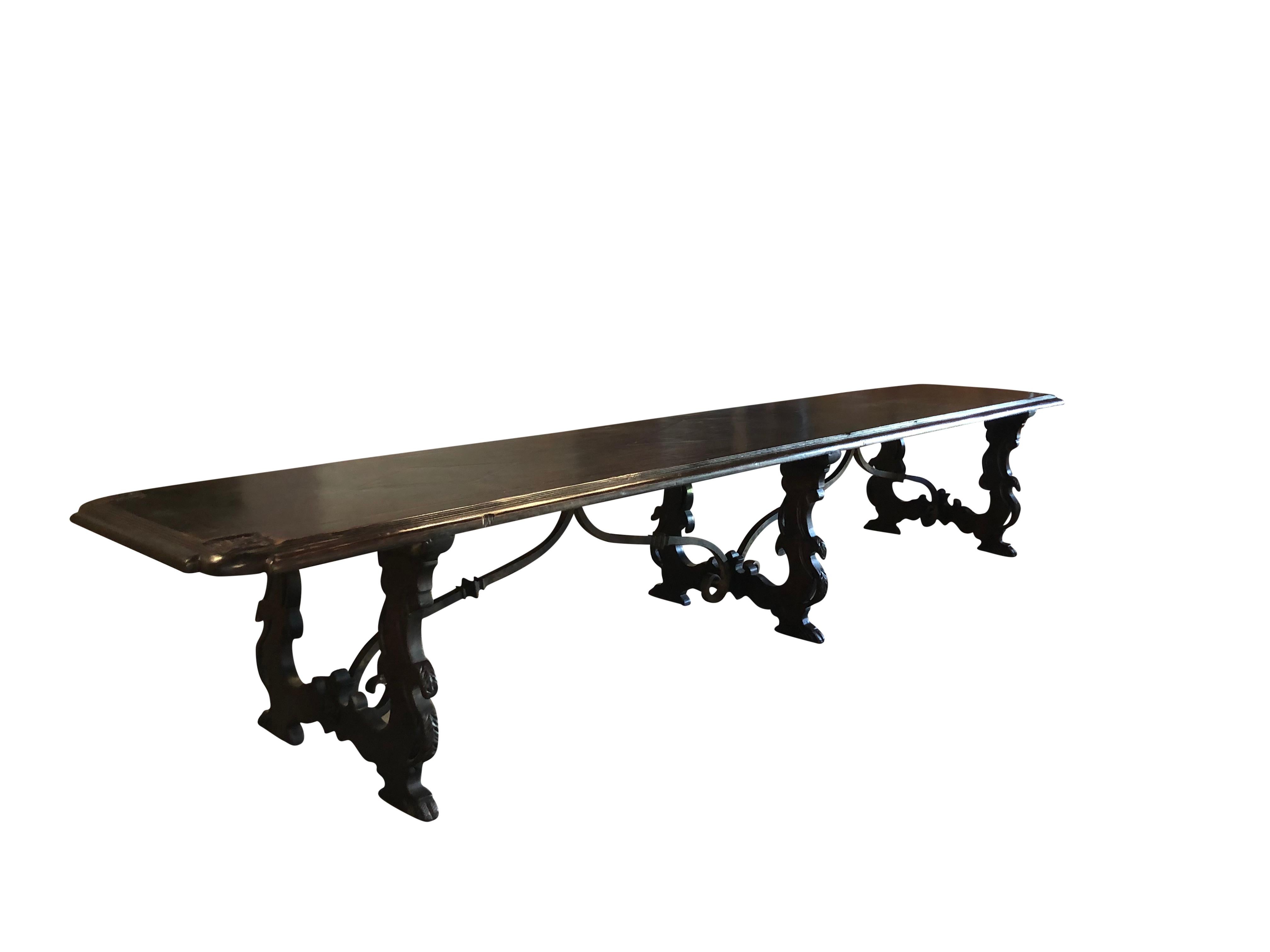 An important and over sized Italian Refectory table. The tabletop was carved by hand in a single dark walnut plank and is adorned with carved plate settings and has a Fleur-de-Lys engraved on each corner. The top is raised on shaped trestle ends and