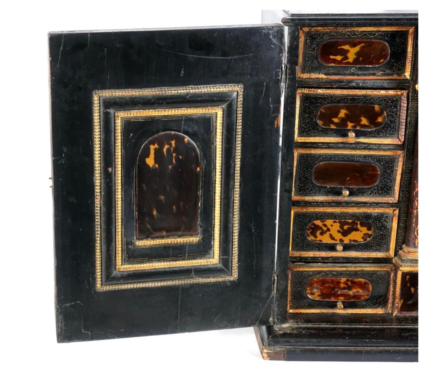 17th century Ebonized case with parcel gilt decoration, iron handles and hinges. Fitted interior with inset tortoiseshell panels surrounded by brass filigree inlaid ebonized wood drawer and door fronts. Faux painted architectural columns on either