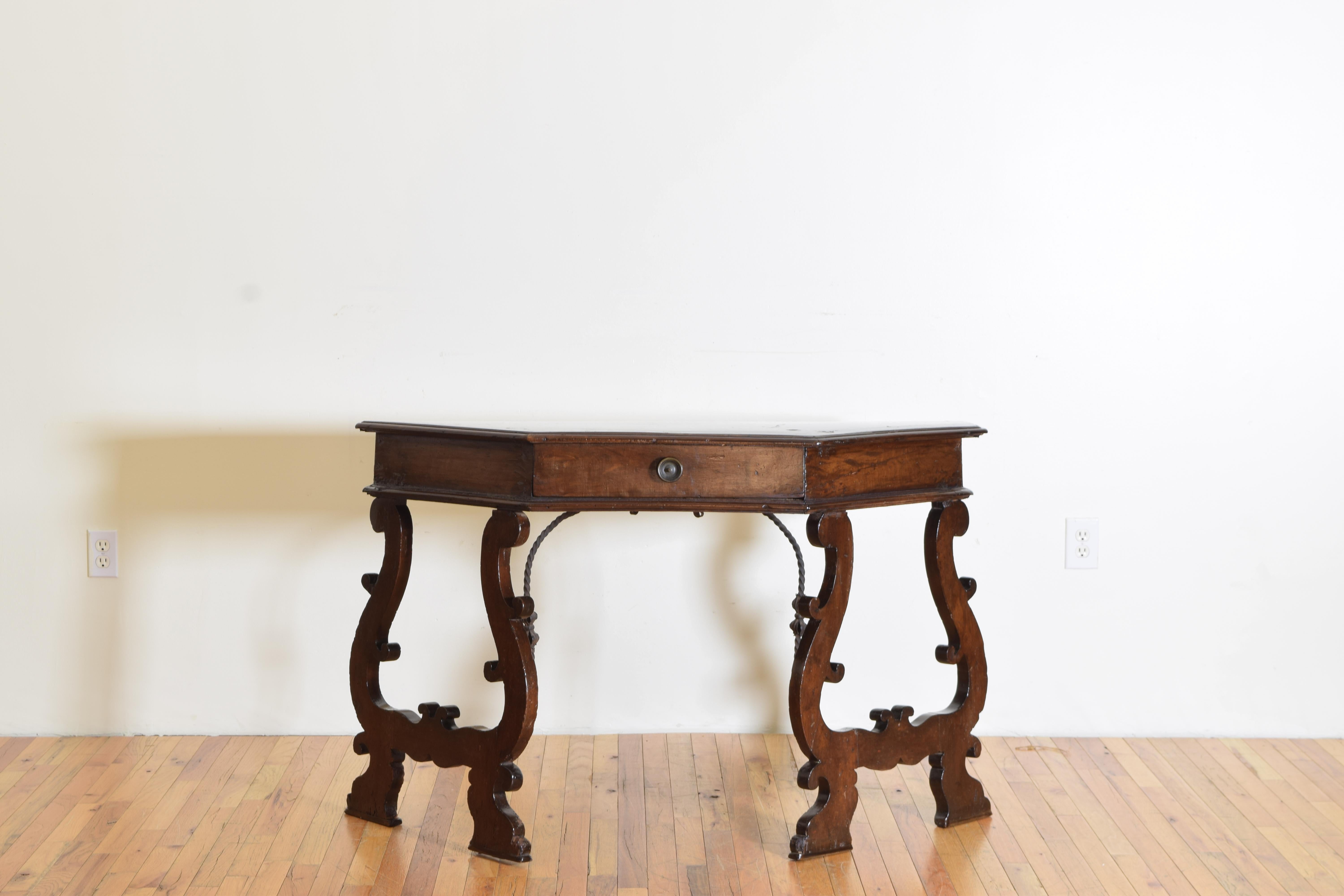 A canted-shaped walnut top with one drawer raised on trestle legs with an iron stretcher support between them with a beautiful aged walnut patina.