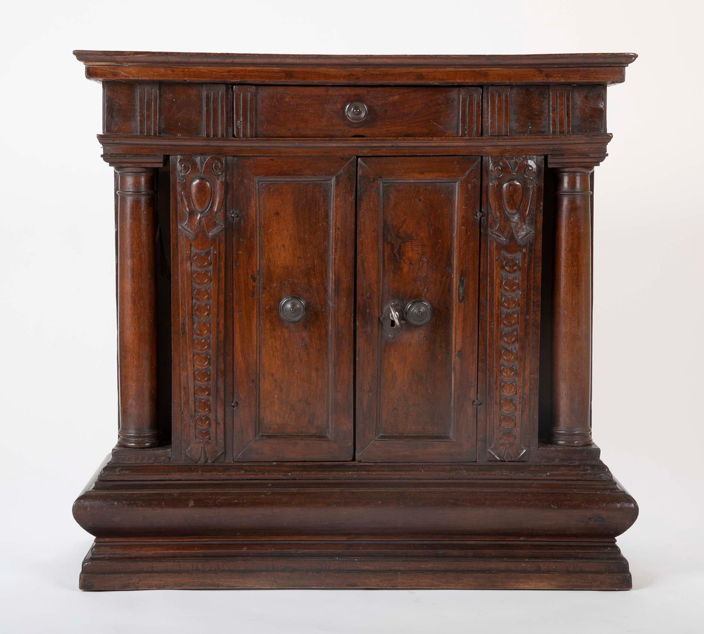 An Italian Baroque Tuscan credenza of classical form with columns carved fully in the round at the corners. A single drawer over a two-door cabinet all with turned bronze pulls. A working key and lock of later date, the interior painted. The walnut