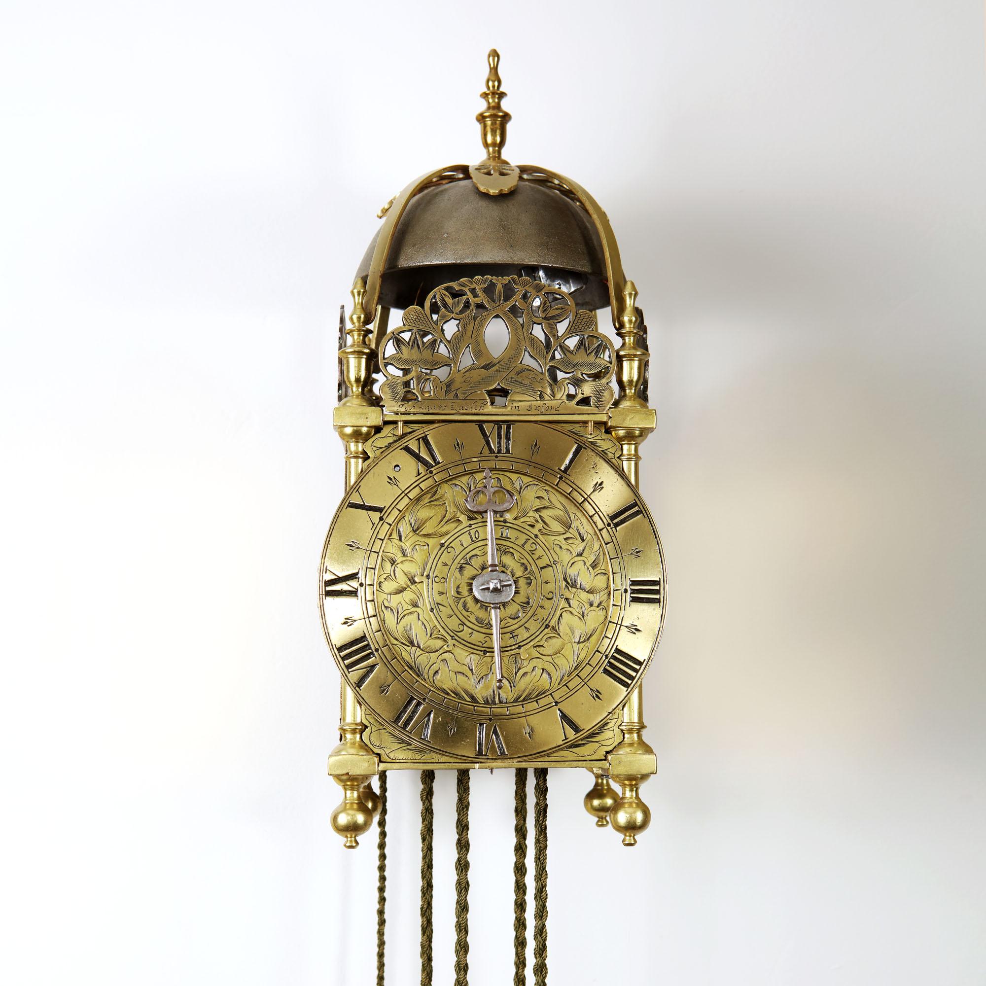 An English 17th century lantern clock made of brass and iron, circa 1665-1670. The clock consists of going and striking trains, as well as an alarm and is driven by lead weights. The front fret shows two engraved dolphins and floral and foliate