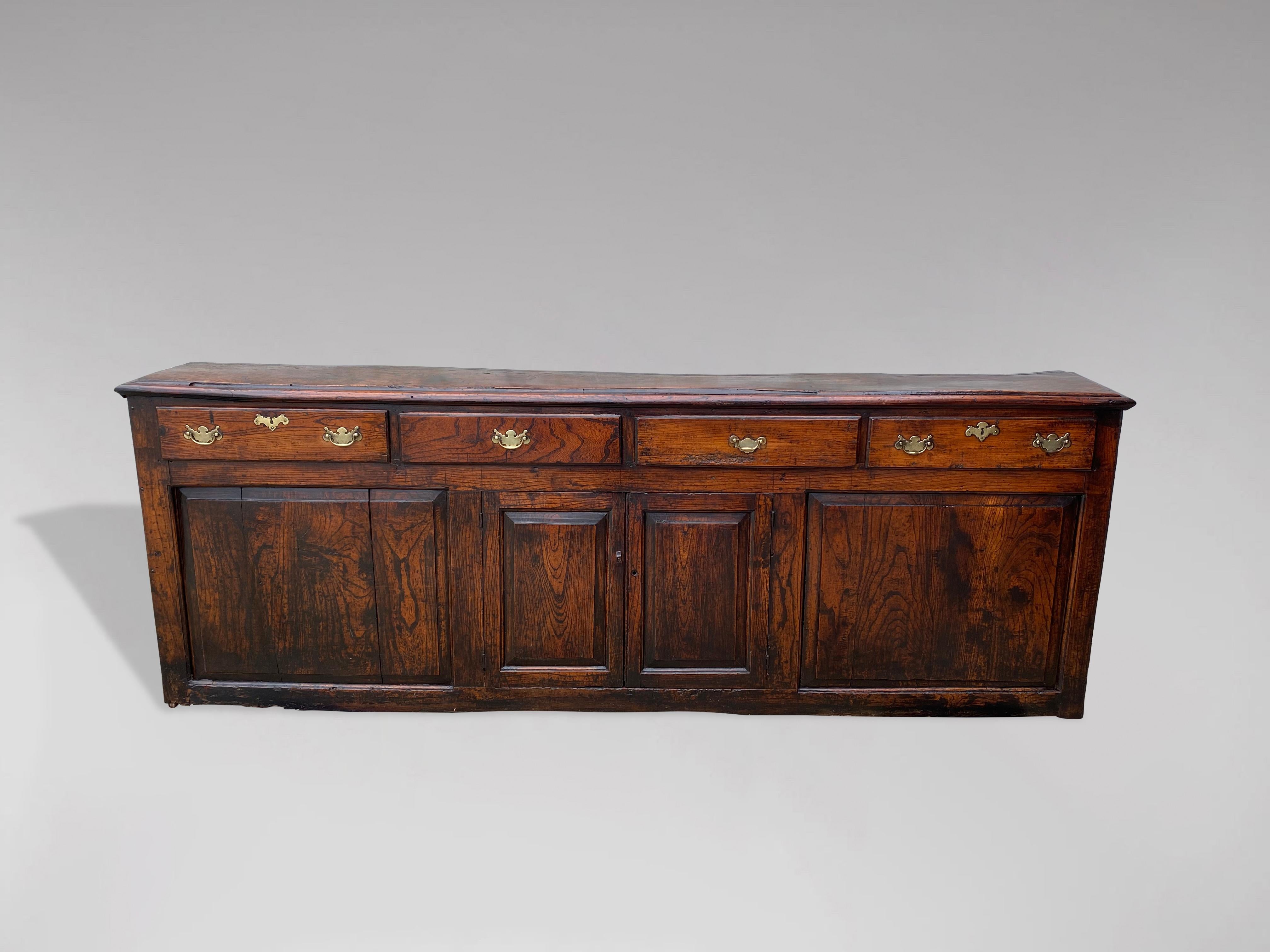 A stunning late 17th century narrow solid oak farmhouse dresser base. Rectangular moulded planked top above 4 drawers with brass handles, above a pair of doors, flanked by 2 large oak panels all standing on a plinth base. Warm rich colour and