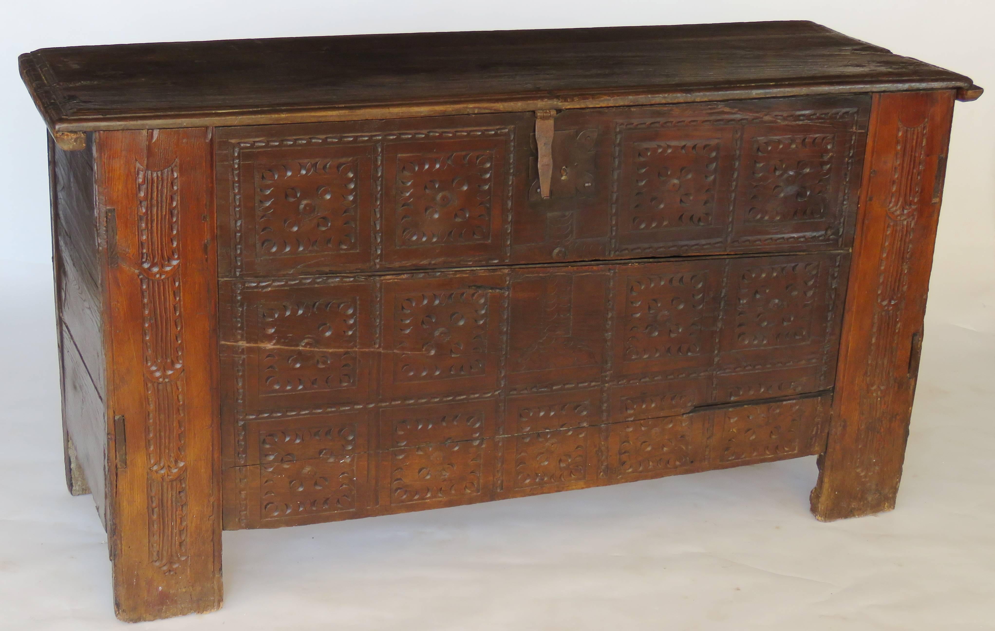 Rectangular hinged molded top over a deeply carved conforming case, front panel with thirteen geometric rosette motifs, centred by large chip carved cross, flanks carved with vertical grooves; original shield lock and hardware.