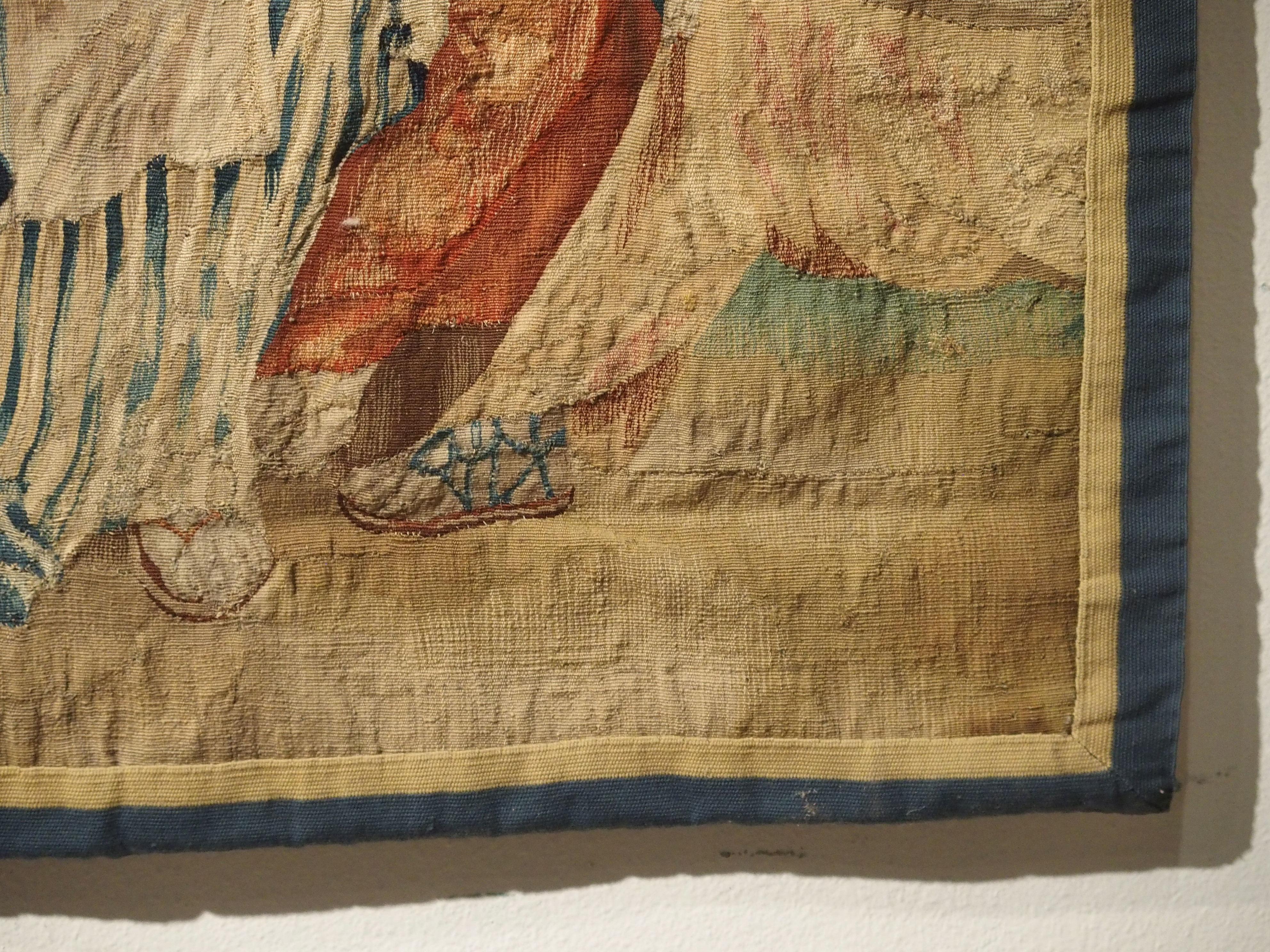 This vibrant antique tapestry fragment is a depiction of two women in a park setting adjacent to a chateau and its grounds. It has been woven in mostly silk, with some wool, and a contemporary two tone border has been added. Unlike many tapestries
