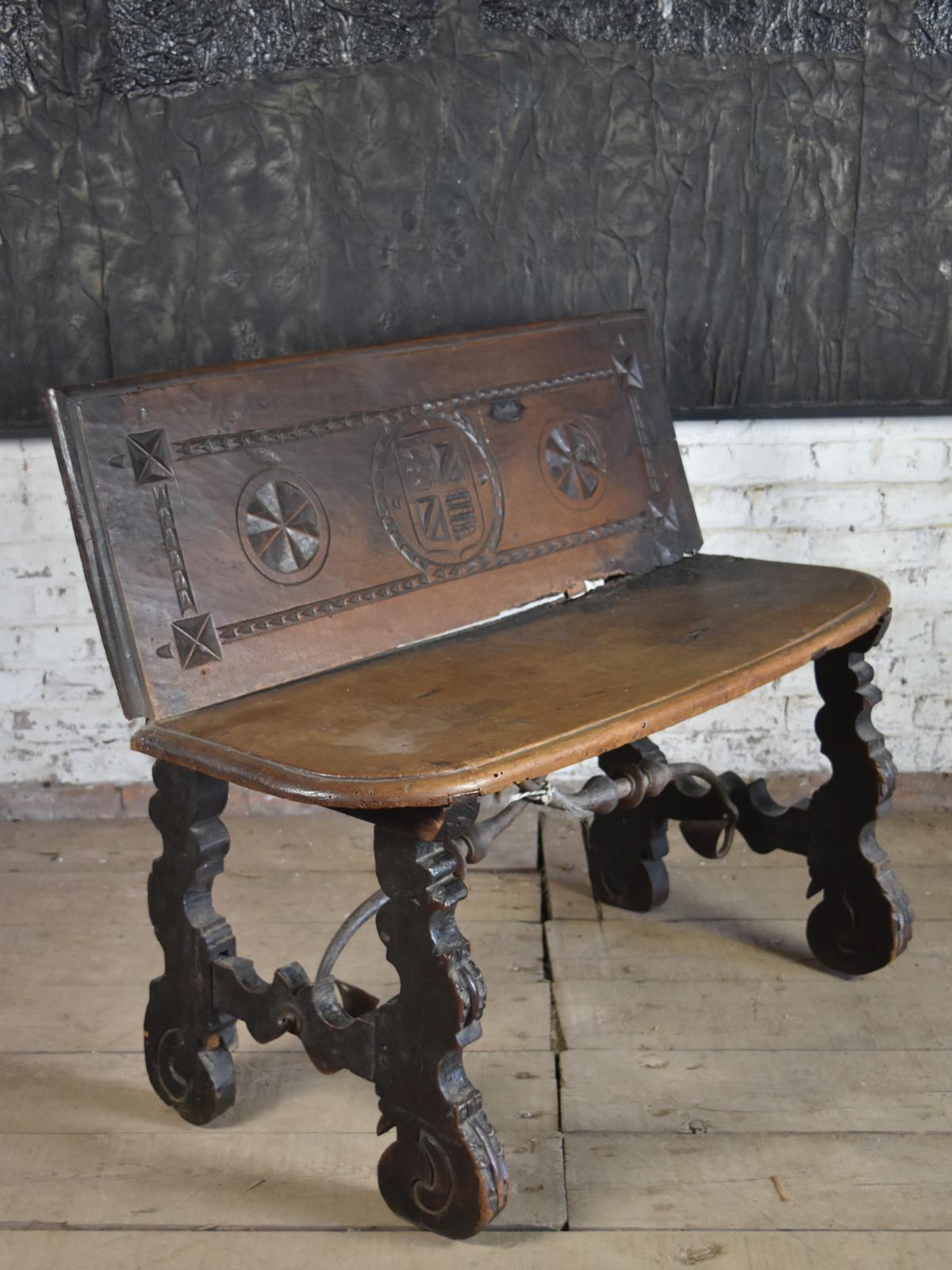 Rustic, Spanish Baroque Walnut Bench of small size (for two people). The back decorated with a carved heraldic shield flanked by geometric roundels and within a chip carved frame. The seat with a molded edge and rounded front corners, supported by