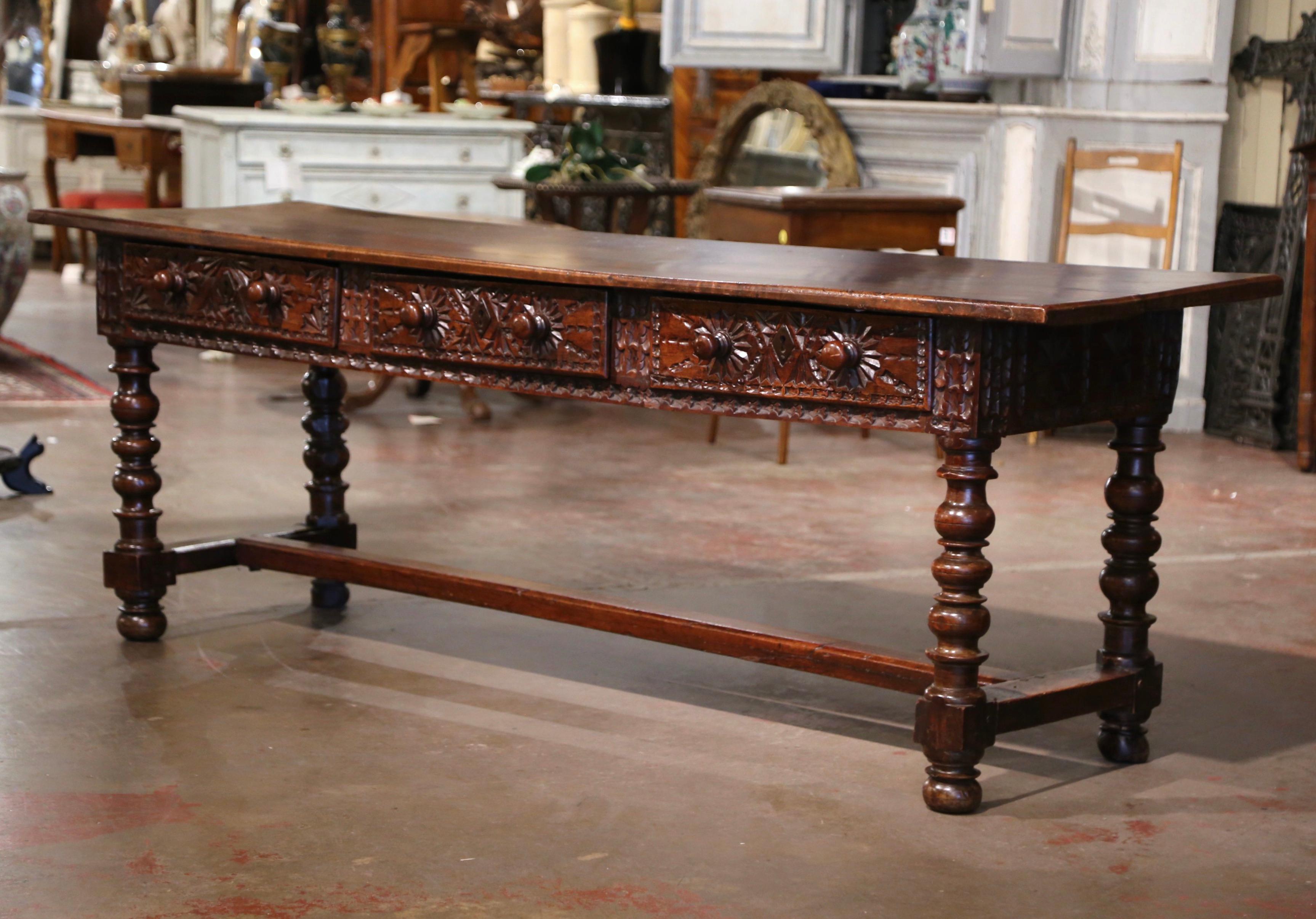 This elegant antique fruitwood Baroque console was crafted in Spain, circa 1680. Carved on all four sides, the long sofa table stands on thick turned legs ending with bun feet over a bottom stretcher at the base. The console features a single plank
