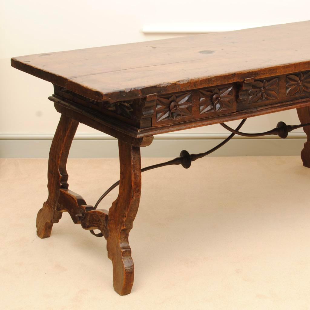 A fine large Spanish walnut table with three drawers to the frieze all with fine carved decoration. The table can be free standing as it has a carved frieze to the rear. With original metalwork stretchers to support the legs.