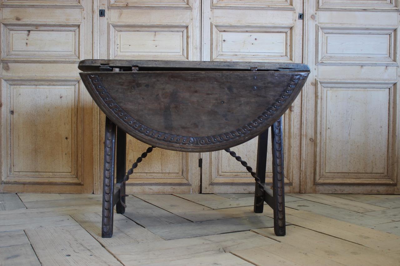 A charming 17th century Spanish walnut and wrought iron drop-leaf table, the oval top carved with guilloche decoration.