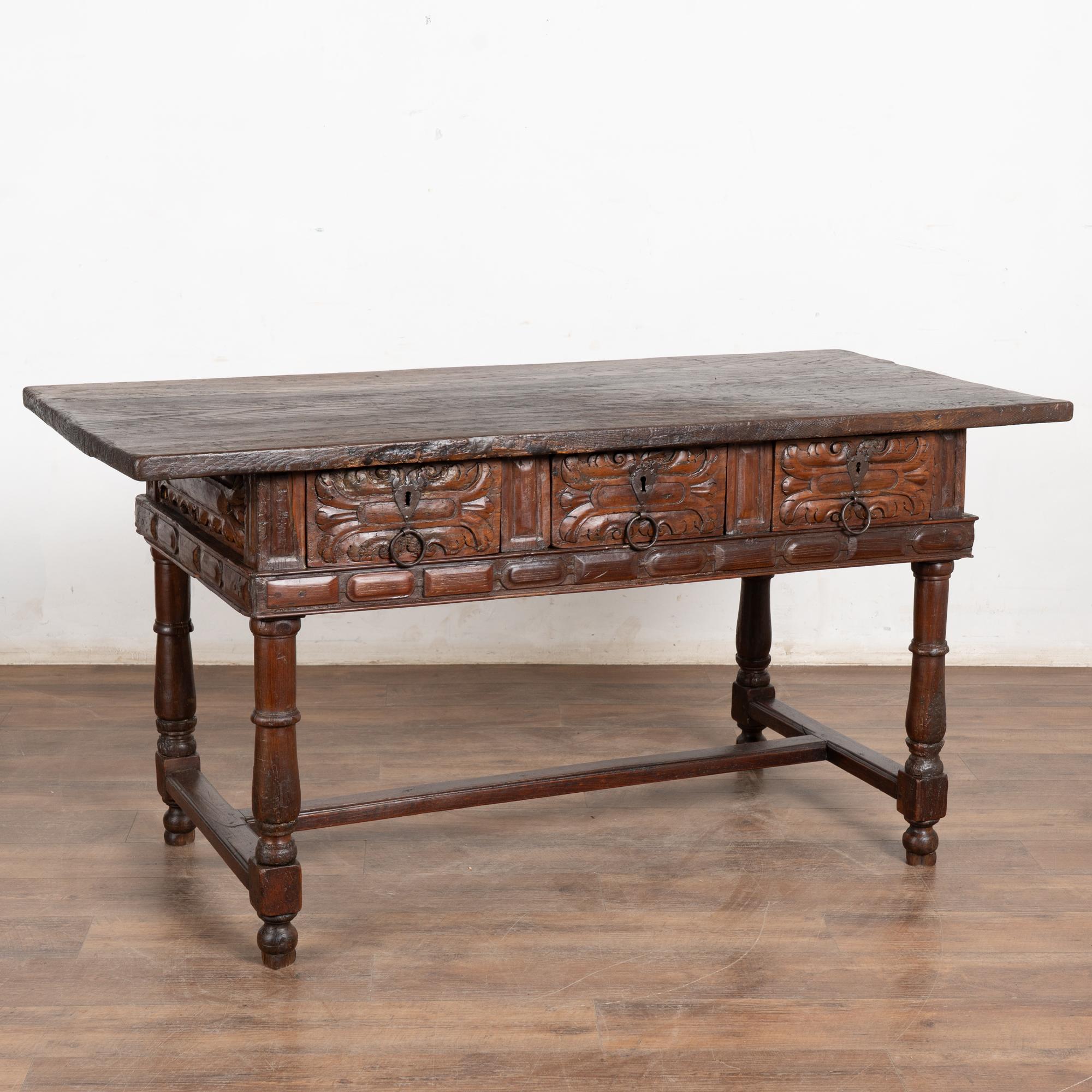 Dark oak console table with three drawers resting on trestle base from Spain. Note the deep carving along each drawer front.
Please enlarge photos (especially of top) to appreciate the dark patina of the wood, including old cracks, gouges, stains