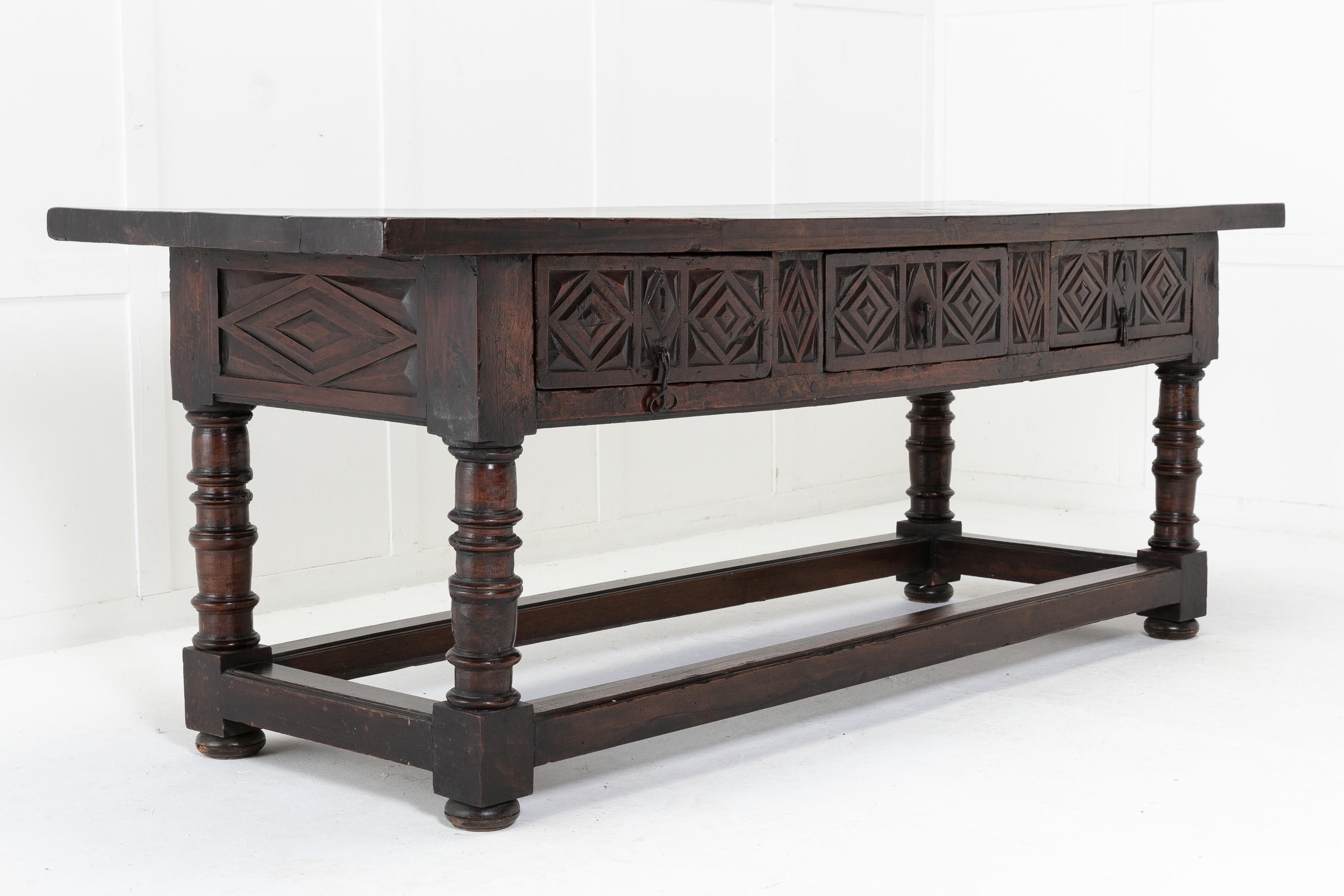 17th century Spanish provincial carved walnut side table with a single plank top above three chip carved frieze drawers creating nice geometric patterns. A substantial table, finished all round. Supported on turned gun barrel legs with peripheral