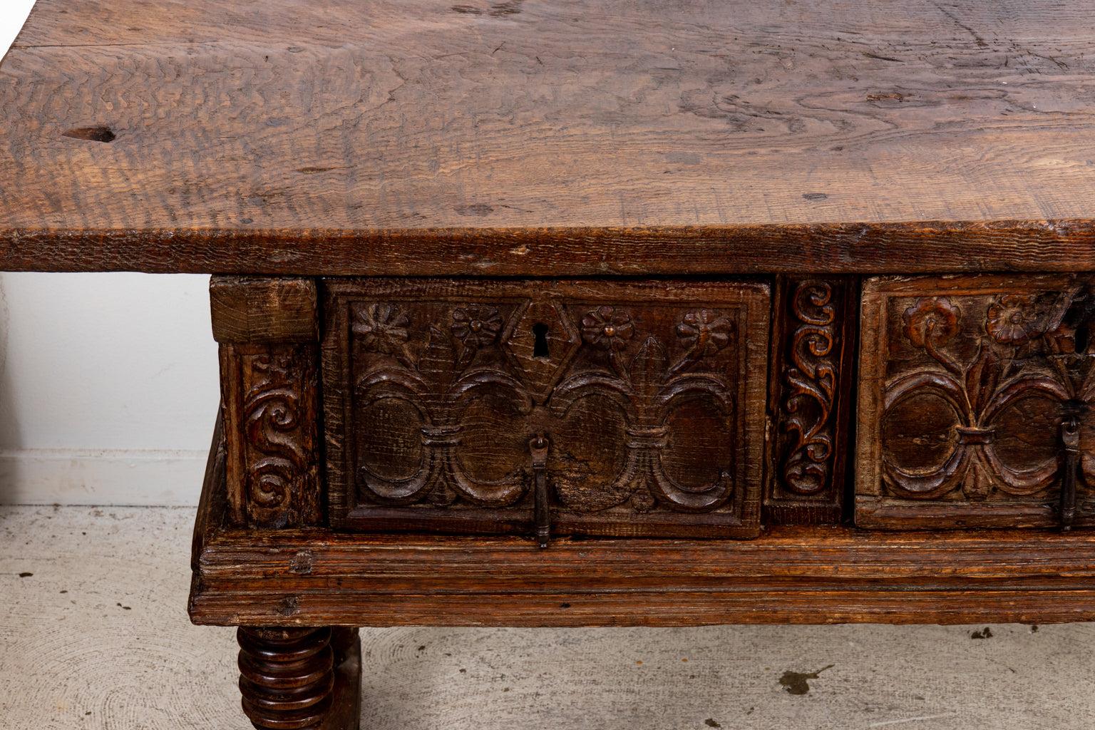 Circa 1690s three drawer table in the Baroque style from the late 17th century with metal hardware. The table is carved throughout with geometric shaped panels, floral motifs, and smaller s-scroll panels. The table is supported by vase-and-ring
