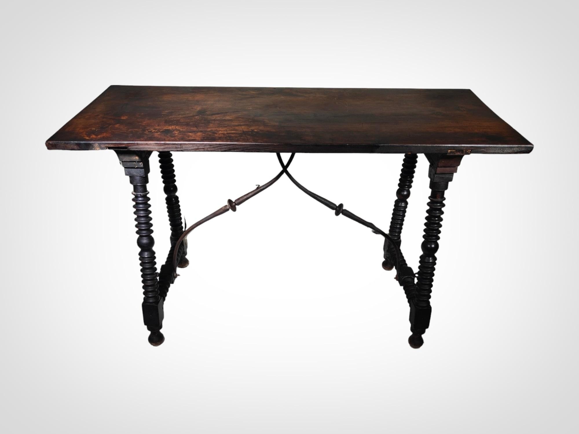 Tauchen Sie ein in die zeitlose Eleganz dieses spanischen Tisches aus dem 17. Jahrhundert, ein wahres Meisterwerk, das die Handwerkskunst dieser Epoche widerspiegelt. Mit seinen gedrechselten Beinen und den kunstvoll geschmiedeten Eisenbeschlägen