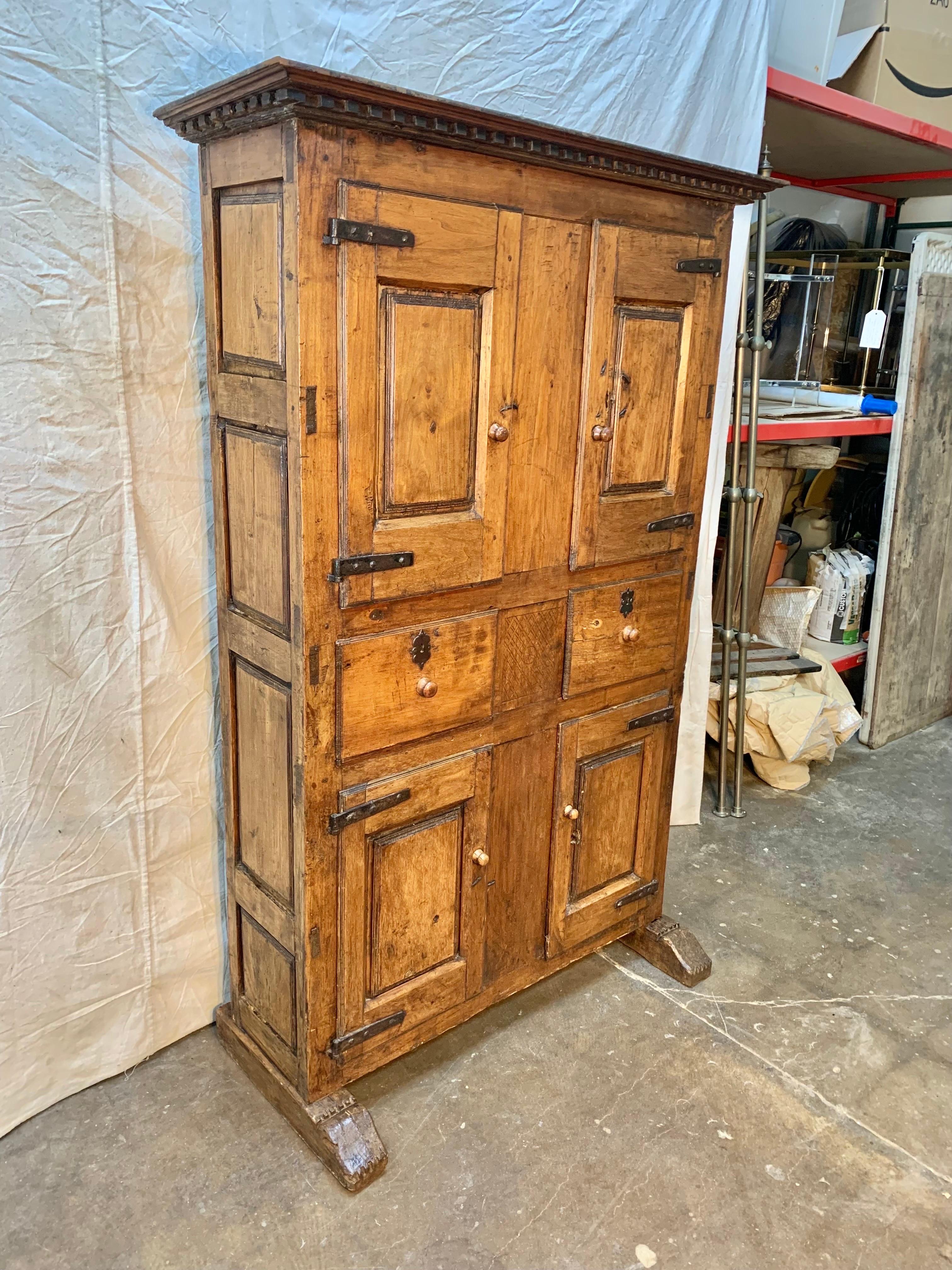 This 17th century Spanish Cabinet was hand carved from old growth walnut. The piece features a hand carved crown over 4 doors and two drawers all raised on hand carved sled feet. The upper and lower cabinet doors have the original hand forged iron