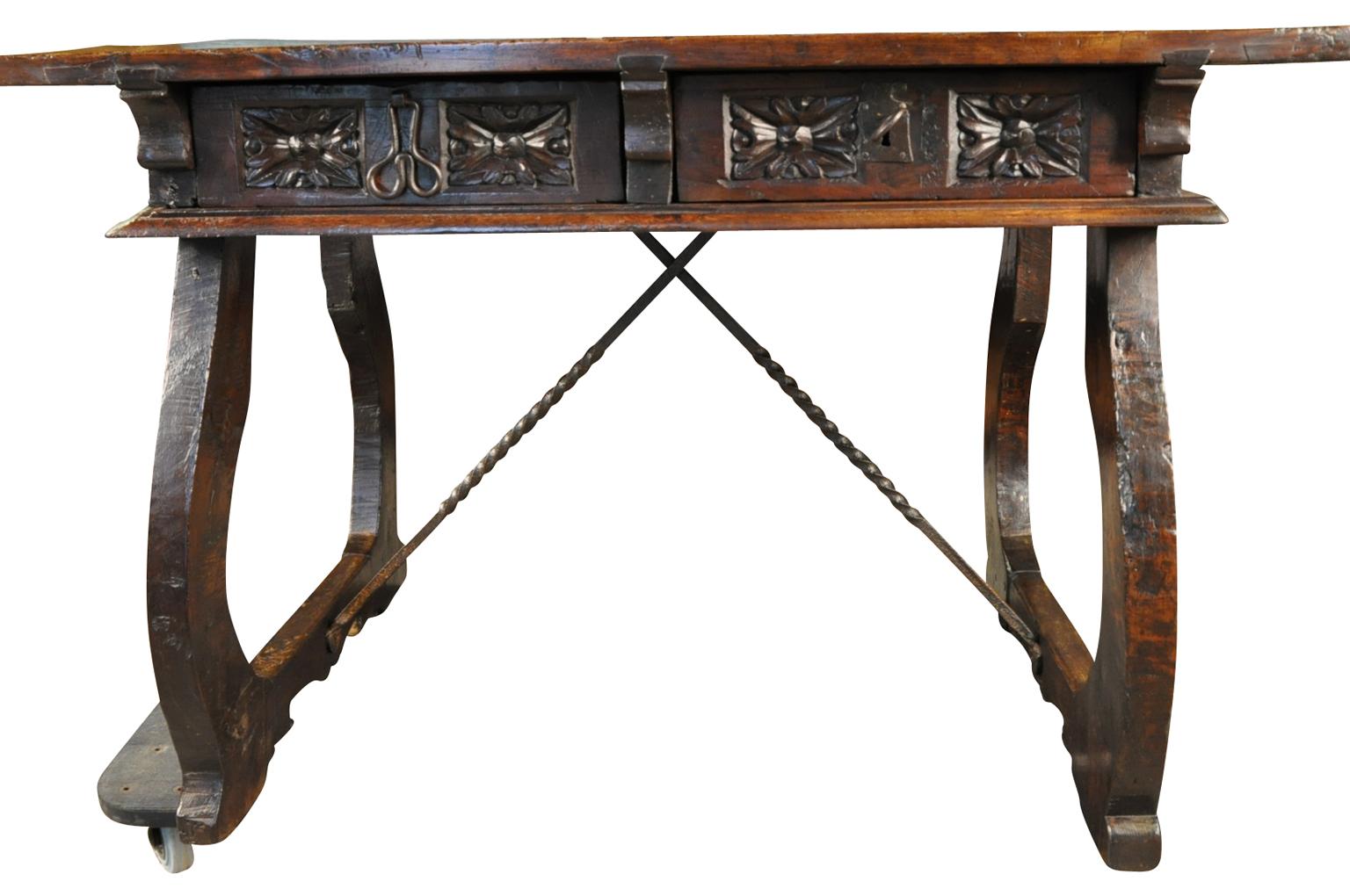 A stunning 17th century writing table from the Navarre region of Spain. Wonderfully constructed from walnut with an outstanding solid board top, classical lyre shaped legs, hand forged iron stretchers, beautifully carved drawer fascias and apron