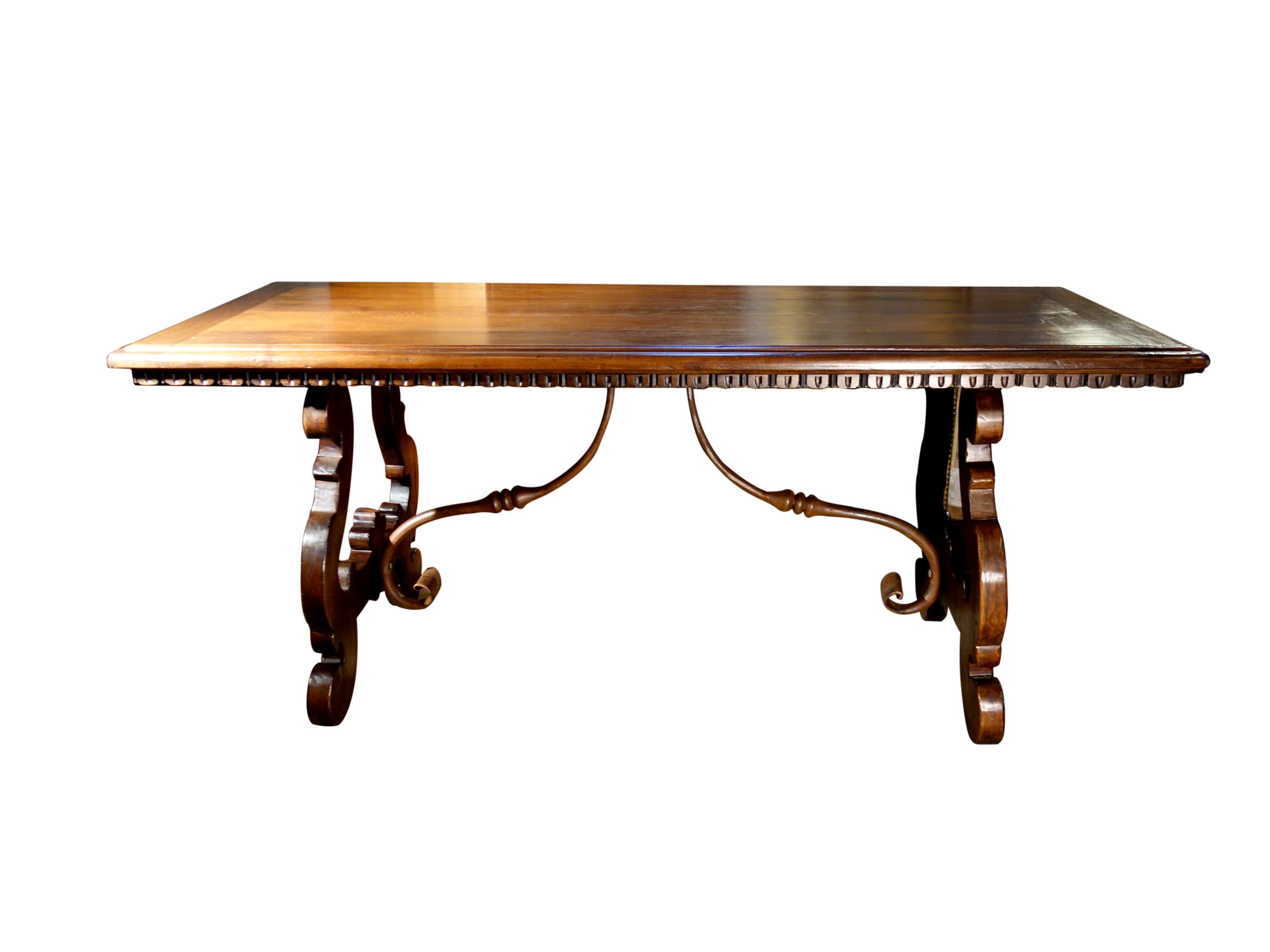 Old Walnut LIRA Scrivania writing table handcrafted in aged solid Italian walnut with a carved dentil edge under the top surface, lyre-shaped bases, and hand forged iron cross stretchers. Our latest 17th Century refectory style antique reproduction
